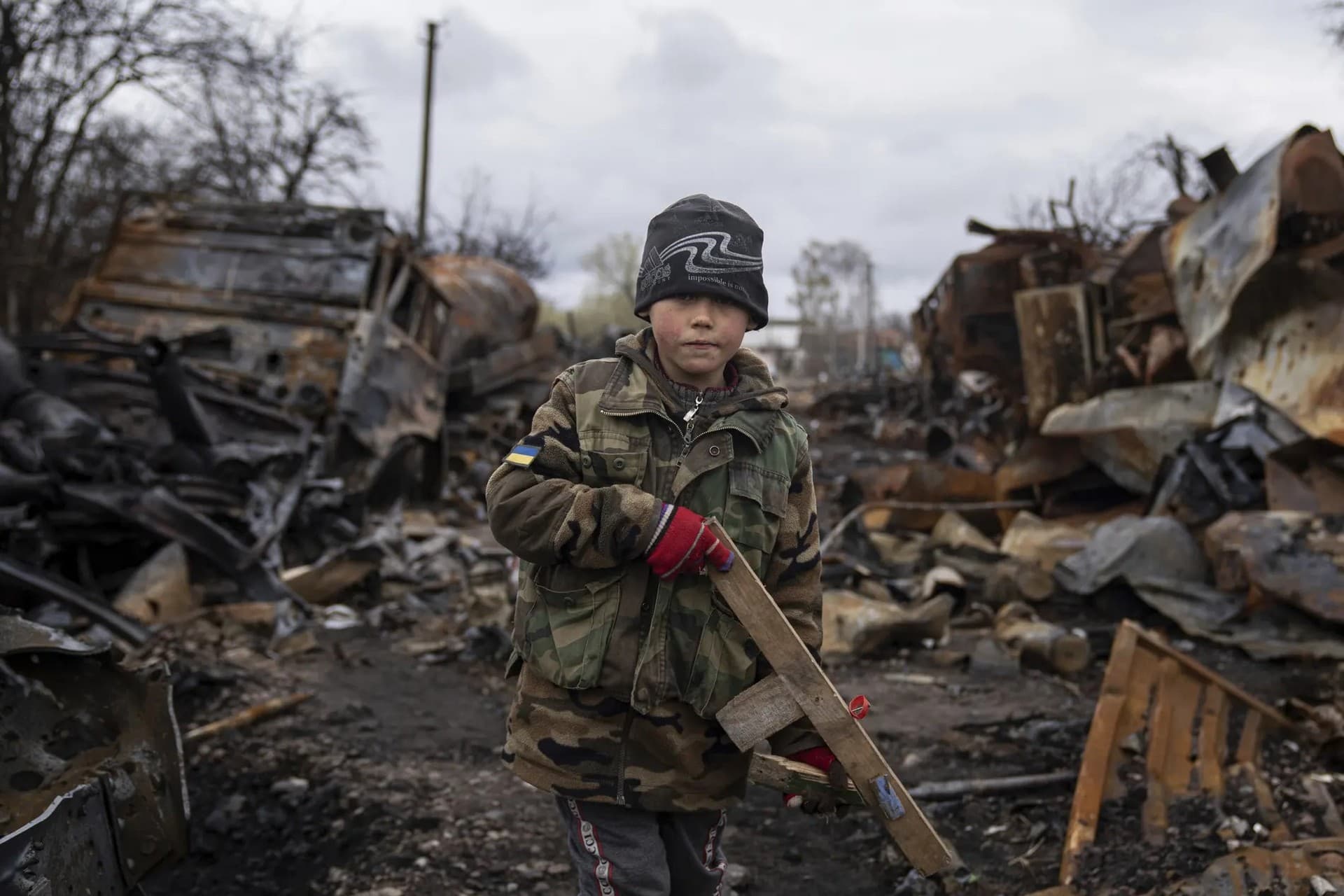 Yehor, seven, holds a wooden toy rifle next to destroyed Russian military vehicles near Chernihiv