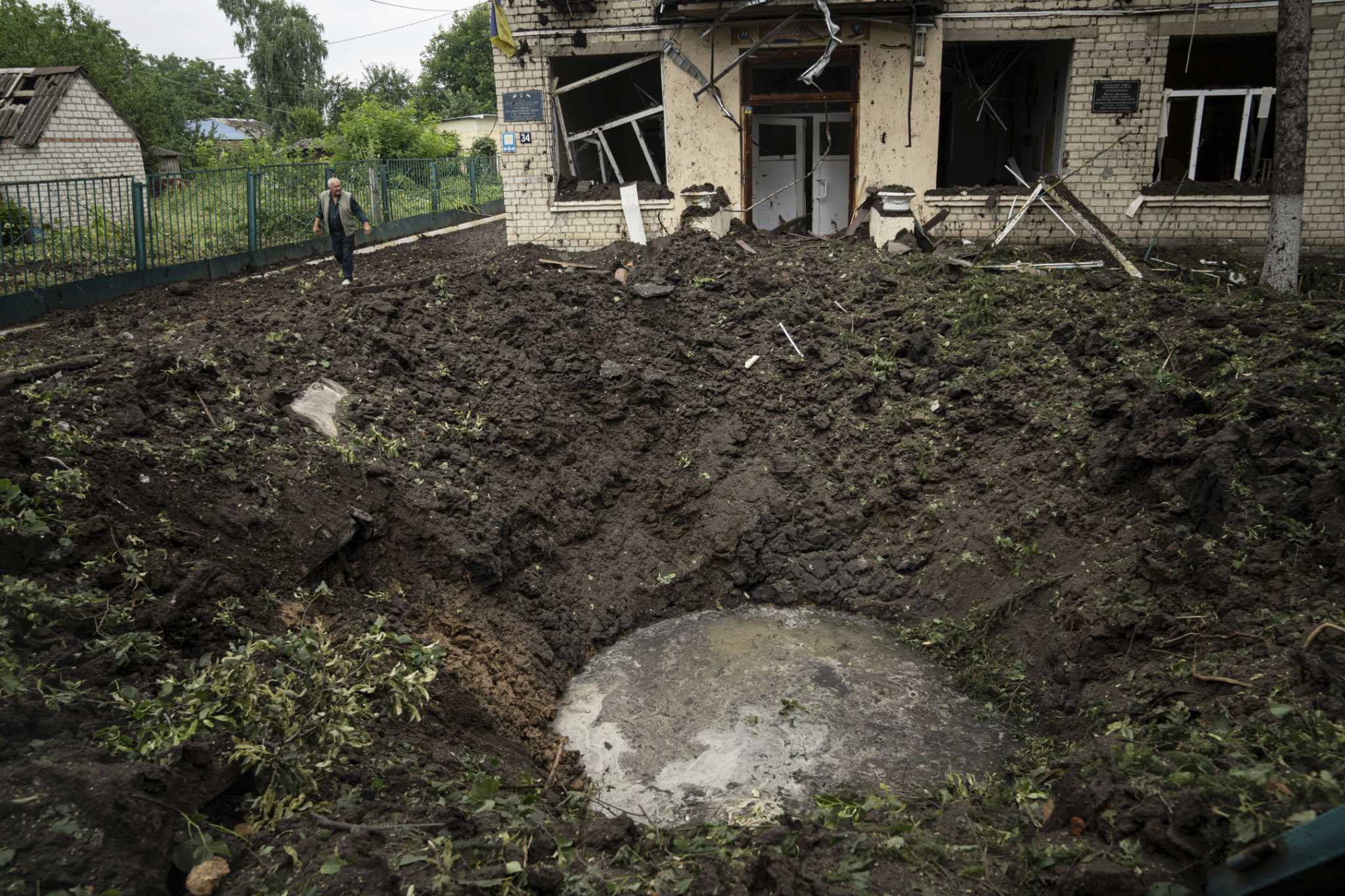 A local man walks in front of a crater and damaged school after Russian shelling at residential area in Chuhuiv