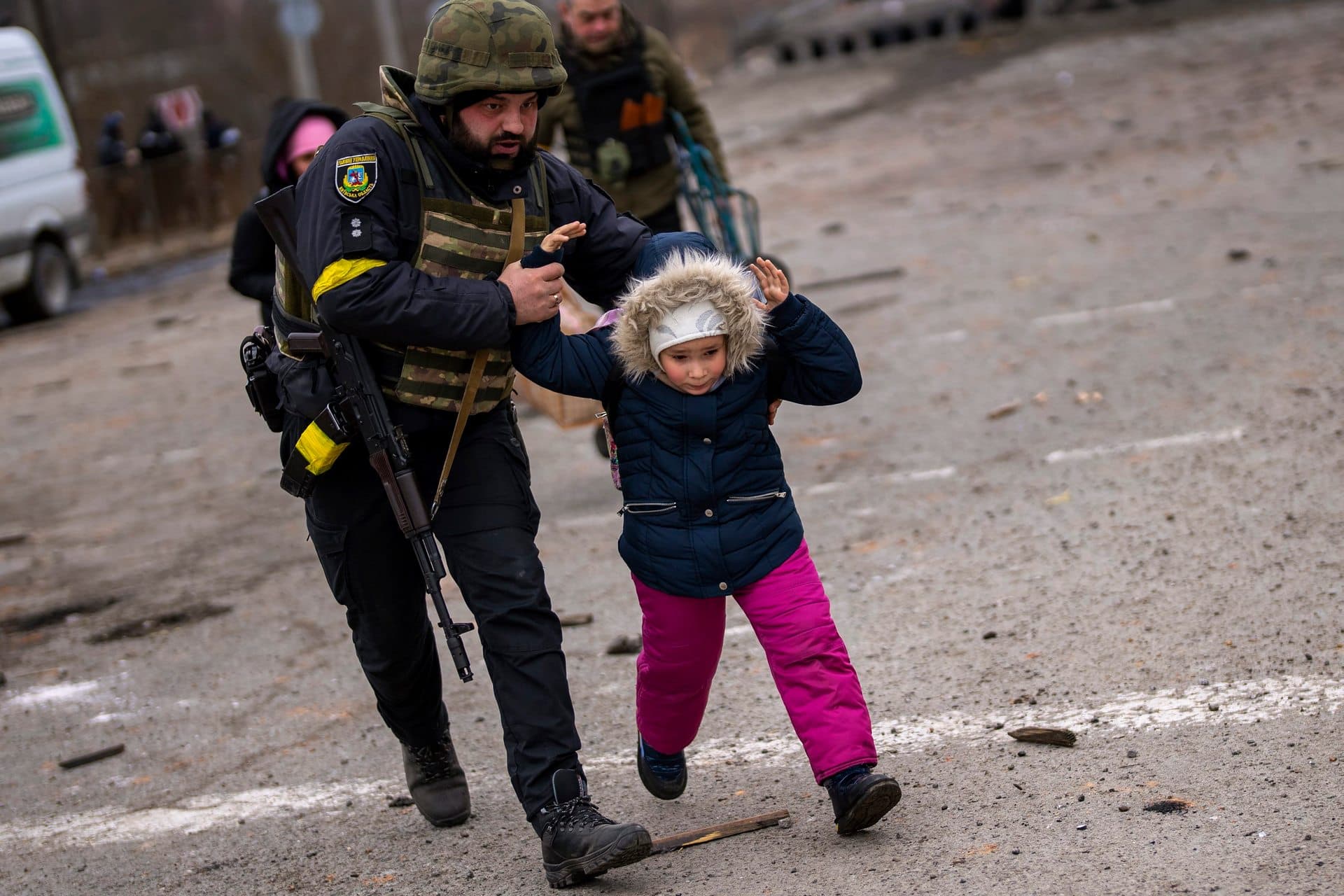 A Ukrainian police officer runs while holding a child as the artillery echoes nearby, while fleeing Irpin