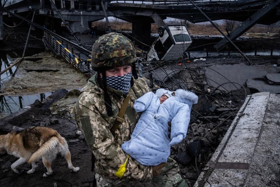 A Ukrainian soldier carries a baby across a destroyed bridge on the outskirts of Kyiv