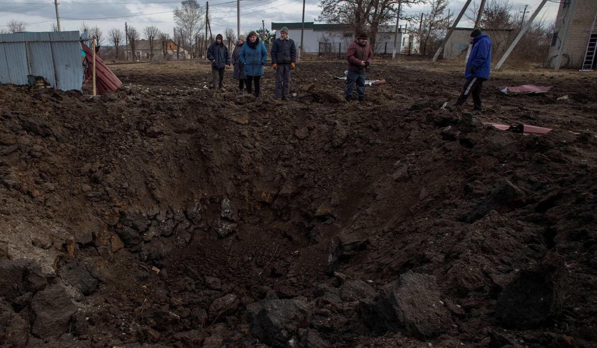 Local residents look at a crater left by a Russian missile strike at a compound of a kindergarten school in the village of Bilokuzmynivka