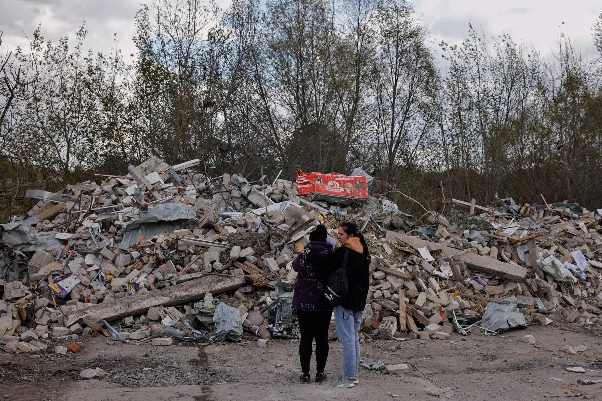 Two women stand in front of a pile of rubble that  is left of the cafe was hit by a Russian missile