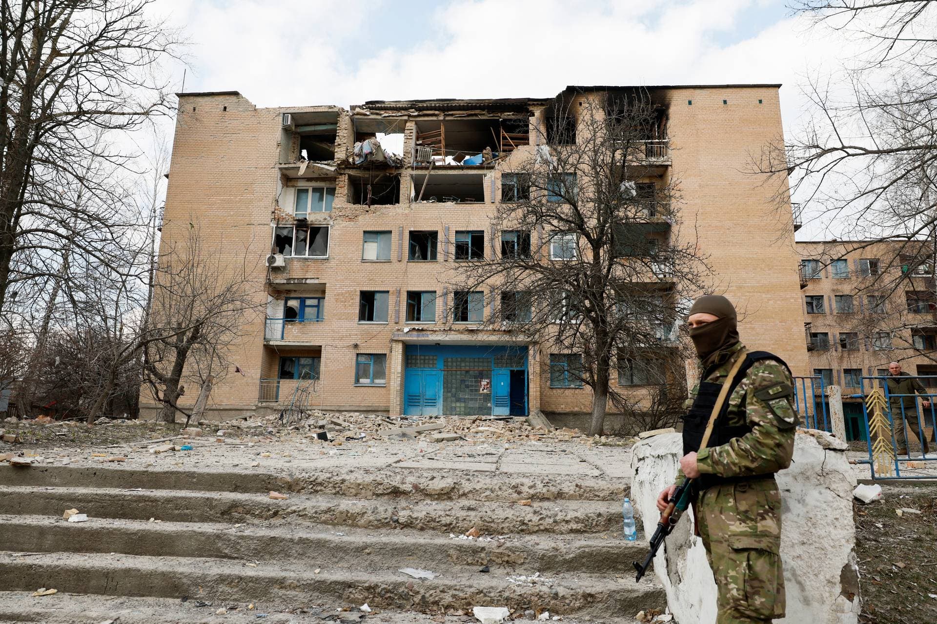 A Ukrainian police officer stands in front of a partially destroyed building after an air strike in the town of Rzhyshchiv