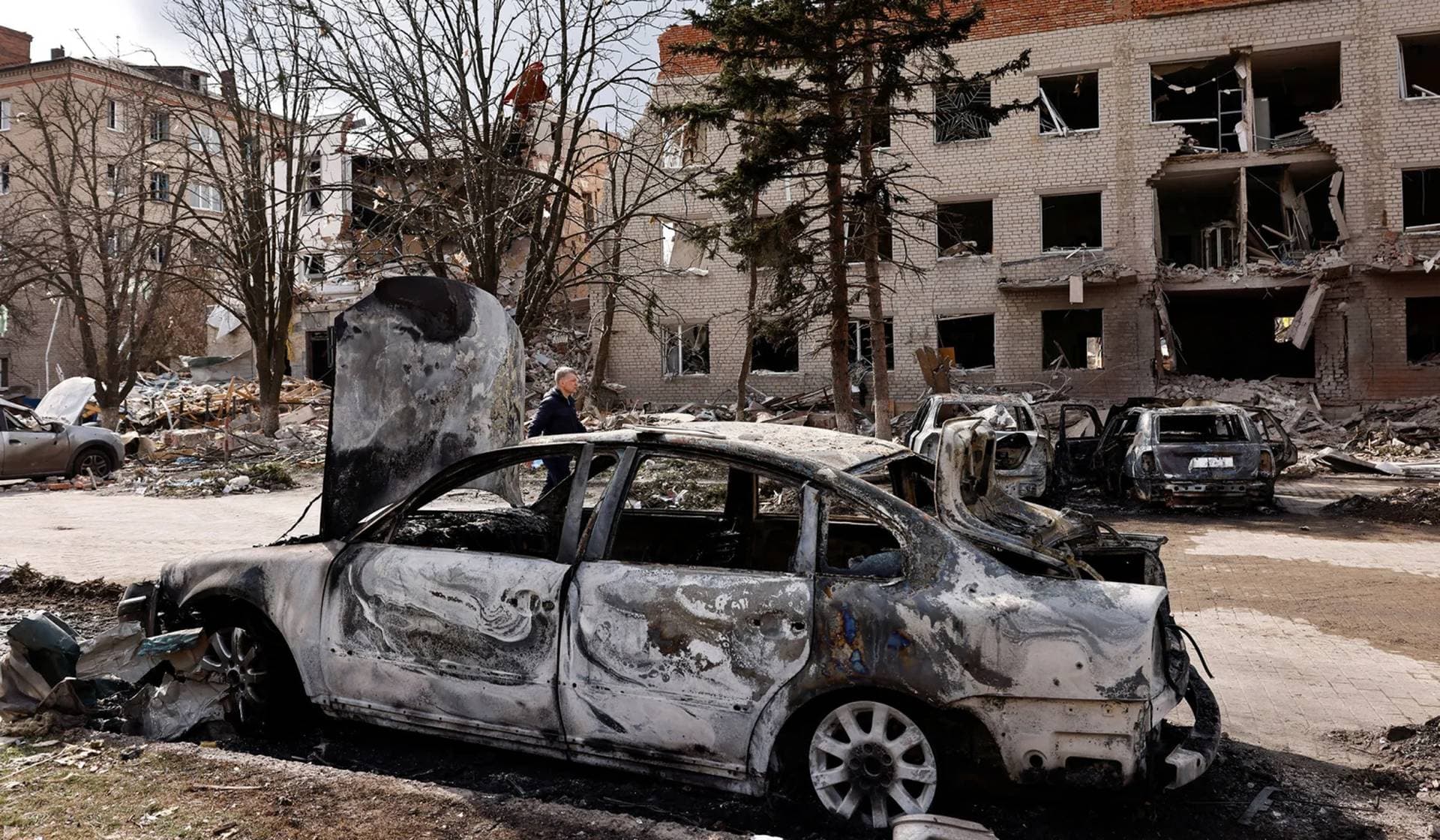 A person walks next to a damaged car in the aftermath of deadly shelling of an army office building in Sloviansk