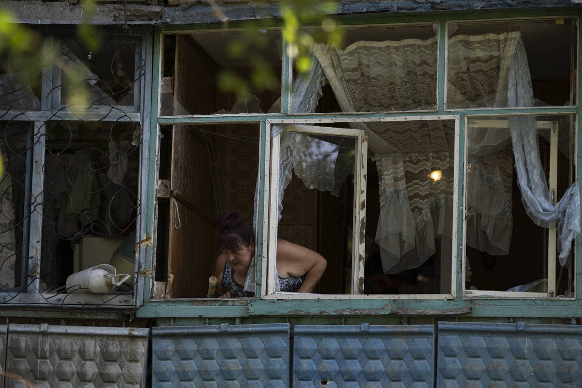 A woman looks out from the damaged window of her apartment after a Russian attack in Sloviansk