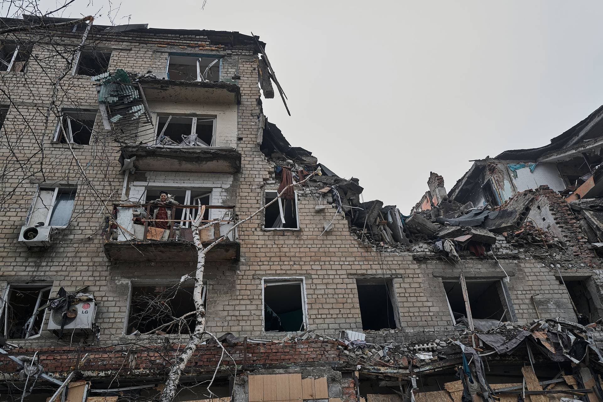 An elderly civilian woman stands with a cat on the balcony of her destroyed house in the Ukrainian city of Avdiivka