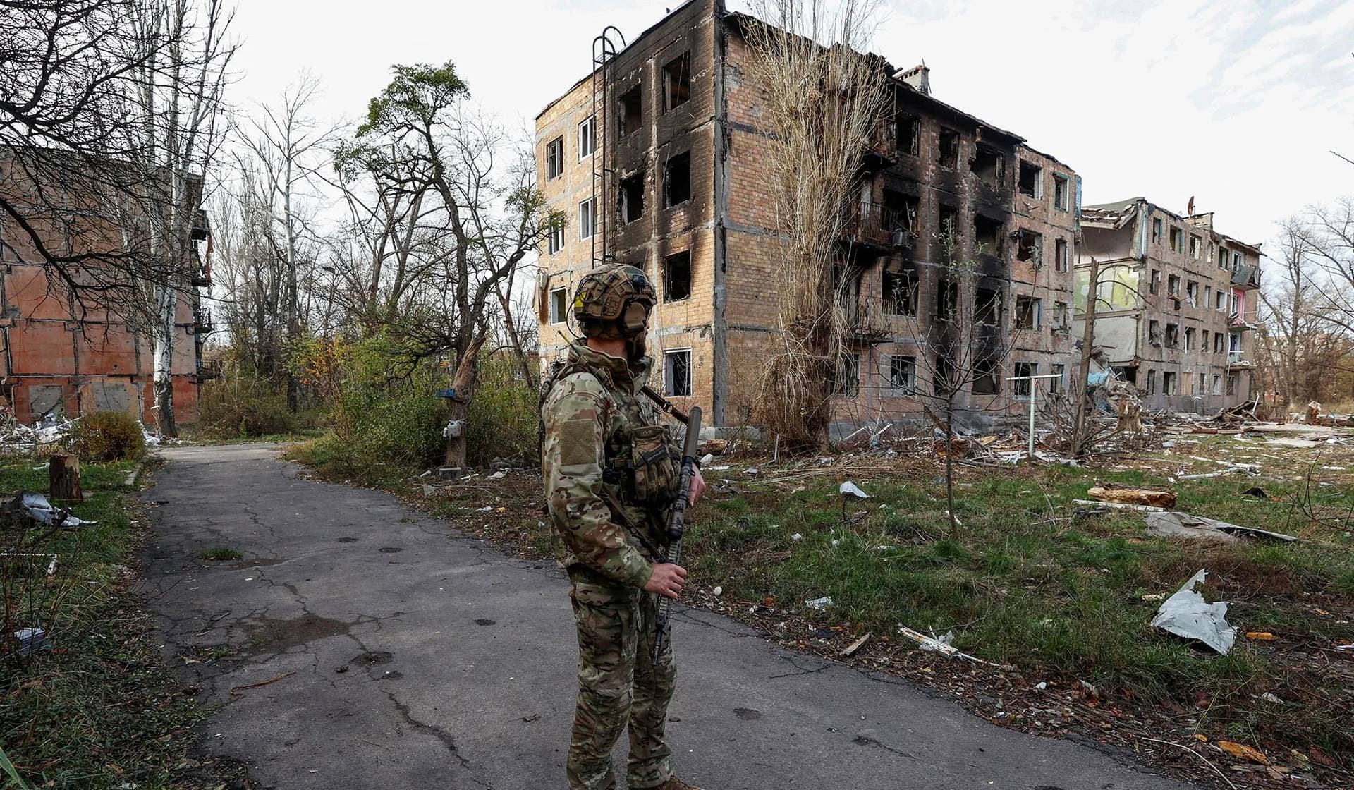 A Ukrainian serviceman stands next to residential buildings heavily damaged by permanent Russian military strikes in Avdiivka