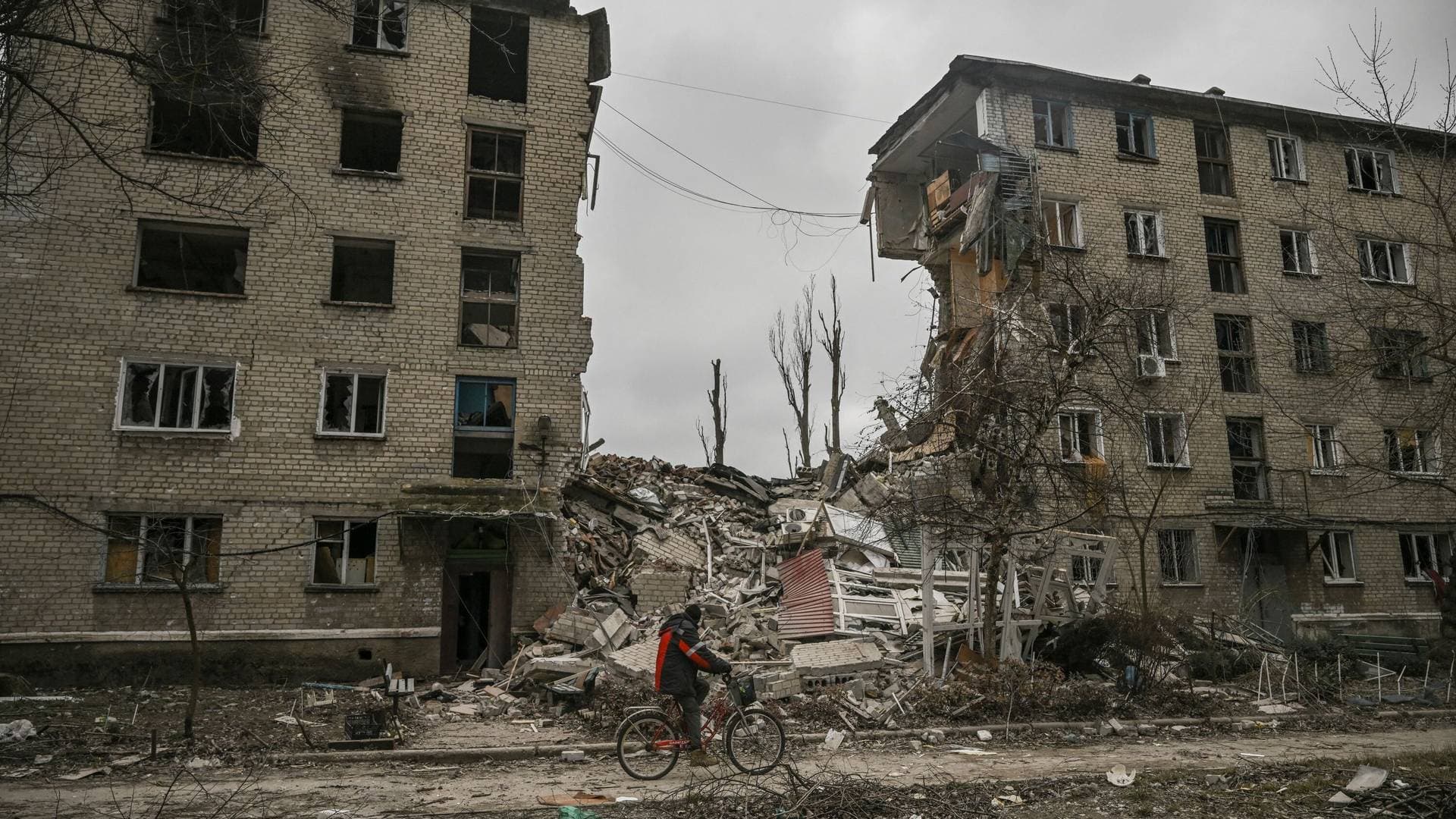 A man rides his bicycle in front of a destroyed apartment building in the city of Avdiivka