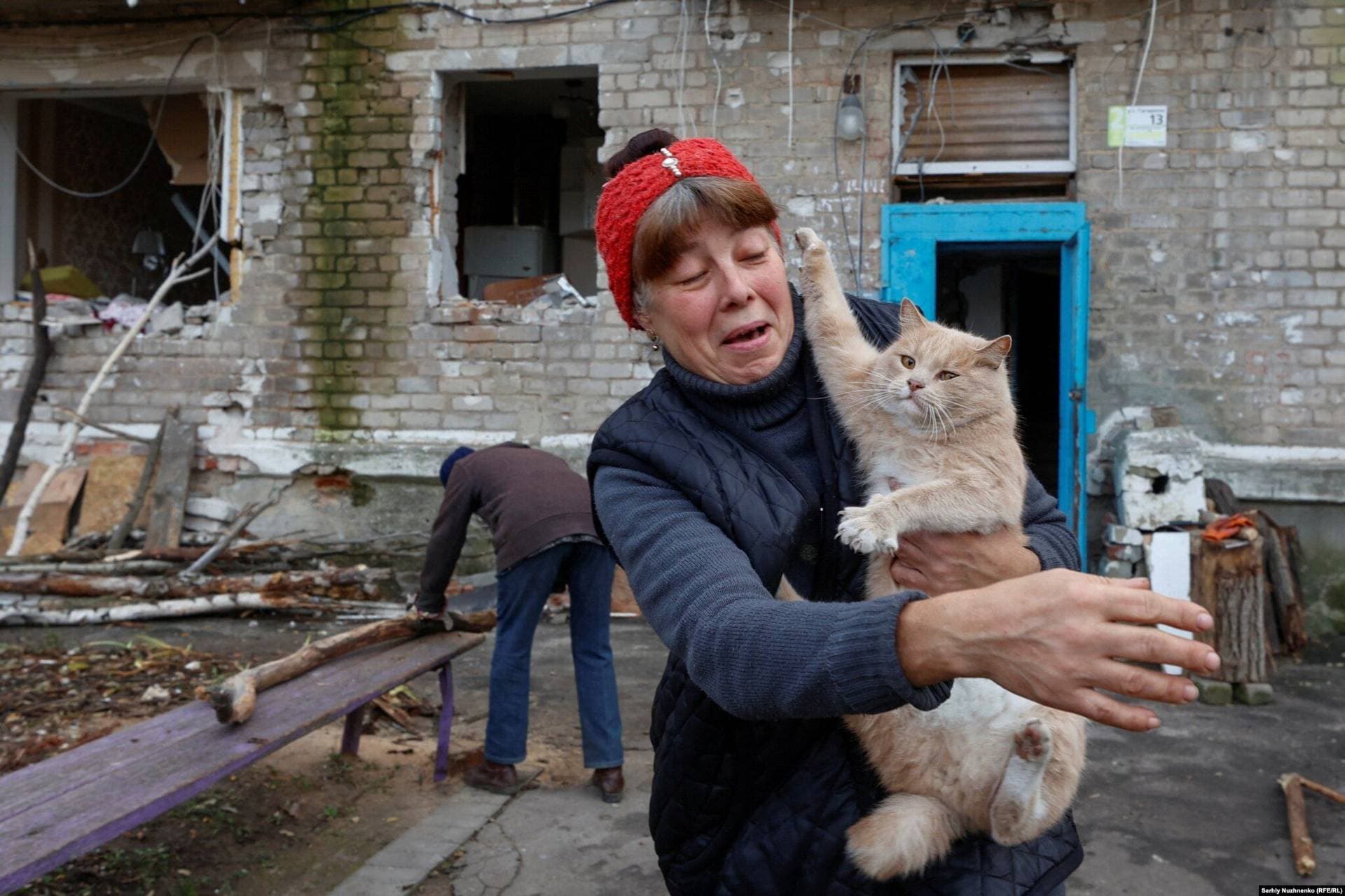 Local resident Rita holds a cat while her neighbor Raisa saws firewood