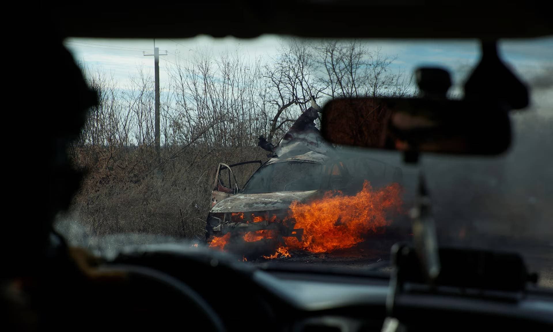 Ukrainian servicemen move past a burning car hit by a kamikaze drone outside the front line town of Avdiivka