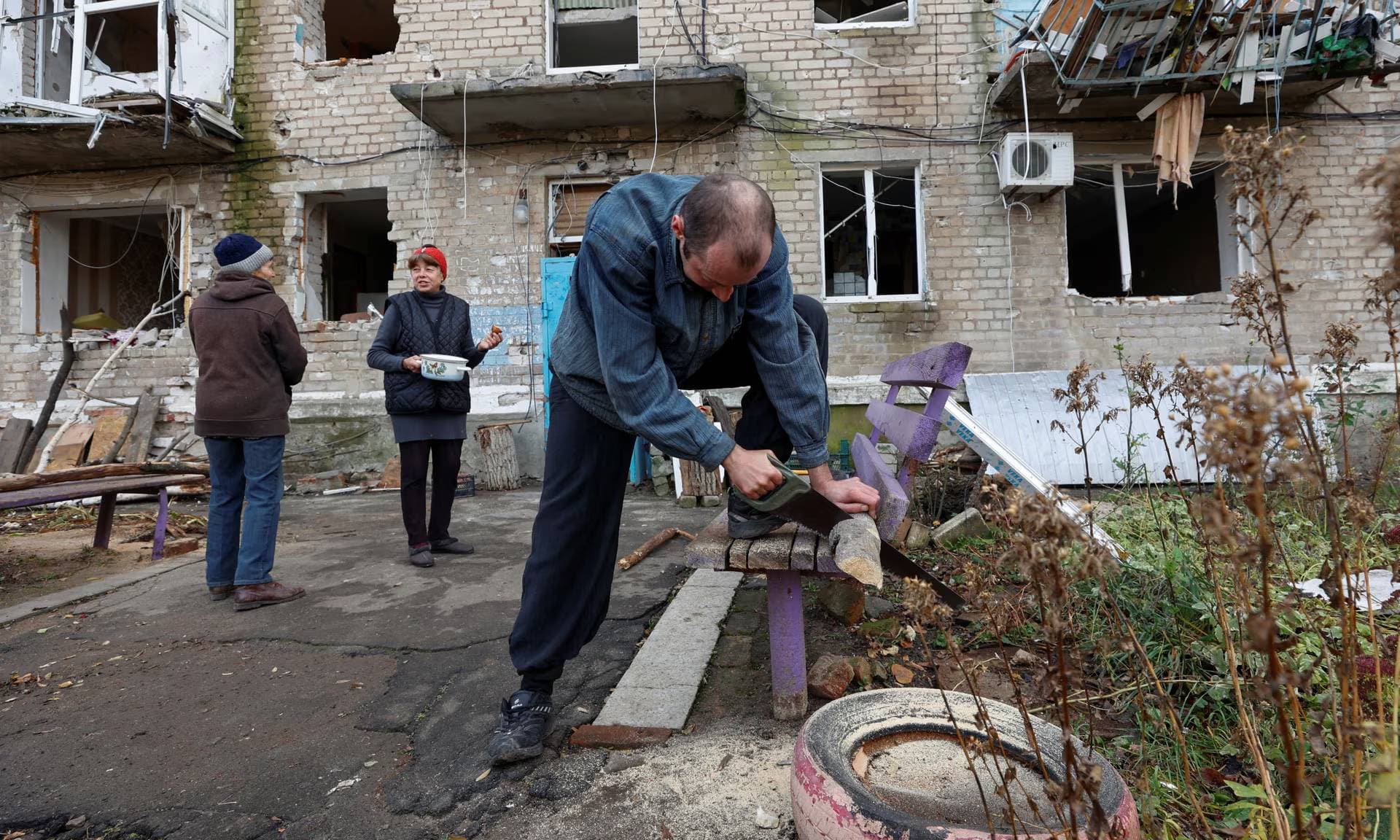 Local resident Oleksandr saws firewood next to his bombed-out apartment building in Avdiivka