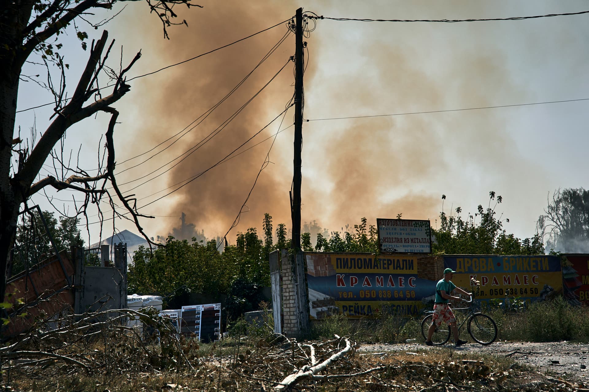 A local resident pushes his bike as smoke rises over the site of an explosion after a rocket attack in Bakhmut