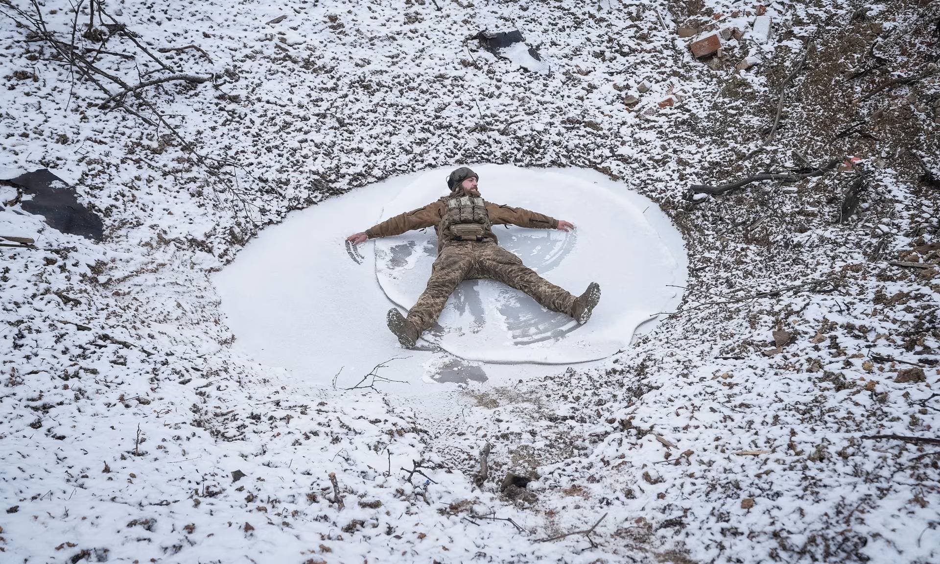 Ukrainian serviceman makes a snow angel in a bomb crater at a position near Bakhmut