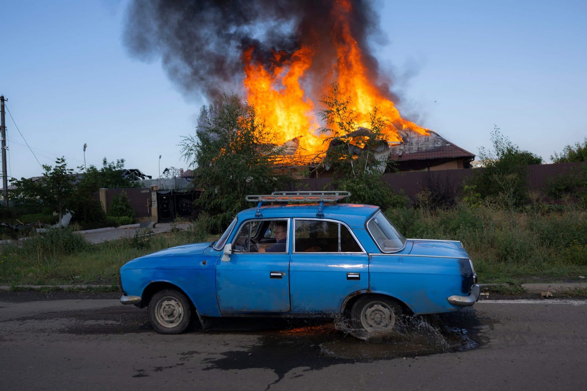 A Ukrainian man drives past a burning house hit by a shell on the outskirts of Bakhmut
