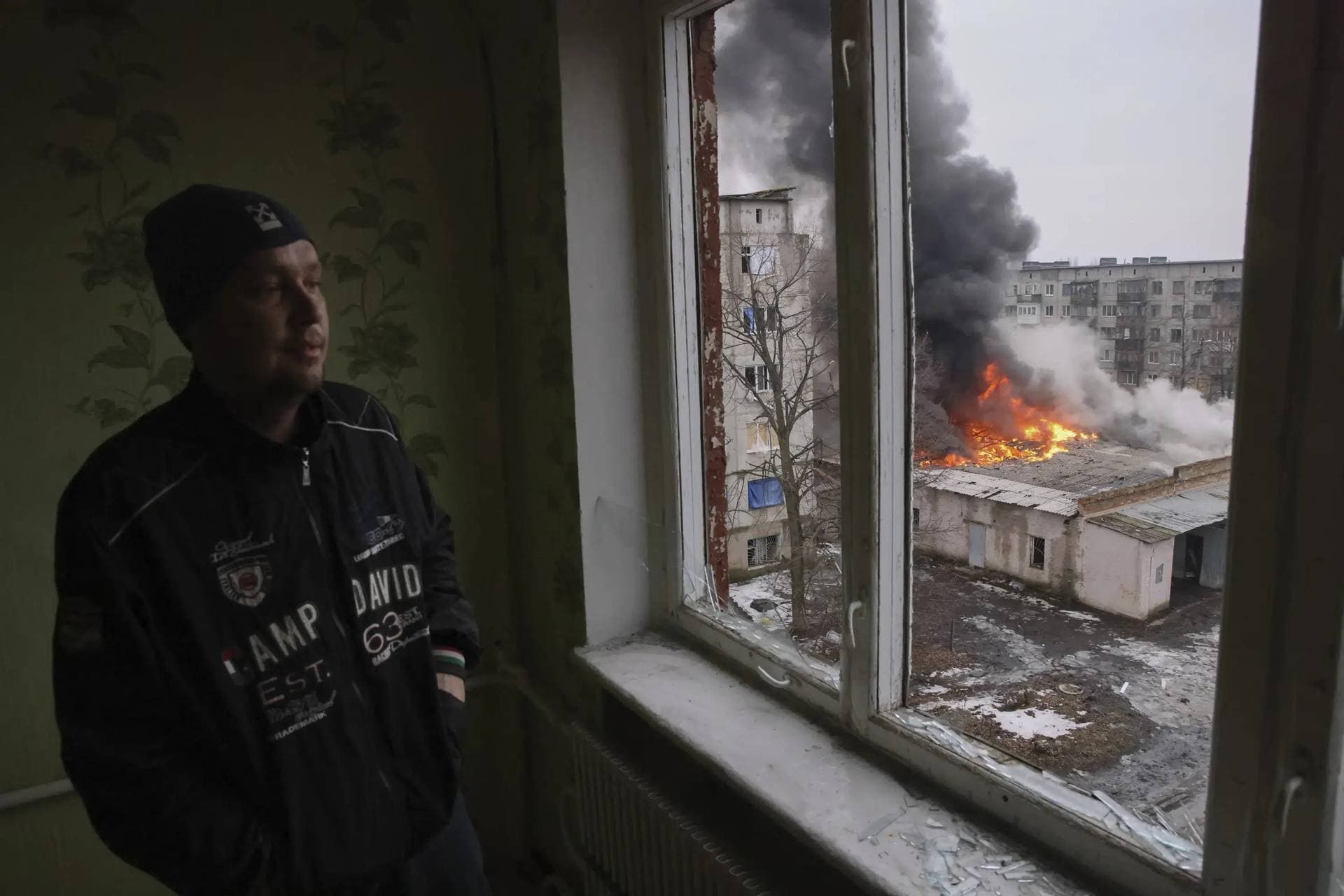A local resident stands at the window as smoke raises from the burning building after the Russian shelling in the town of Chasiv Yar