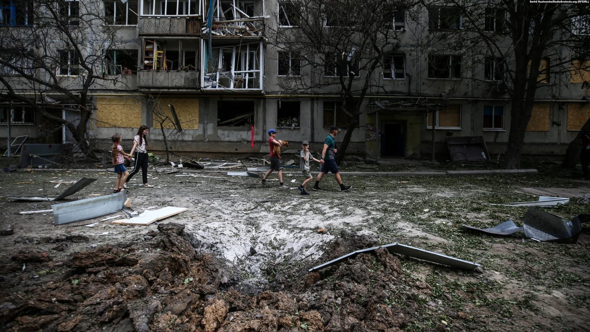 A group of children walks past the remains of a missile strike