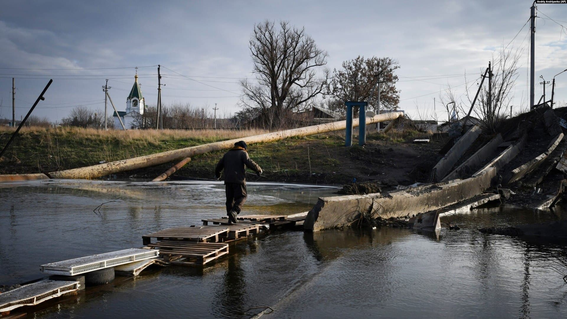 A man crosses a river on the debris of a damaged bridge in the town of Bakhmut