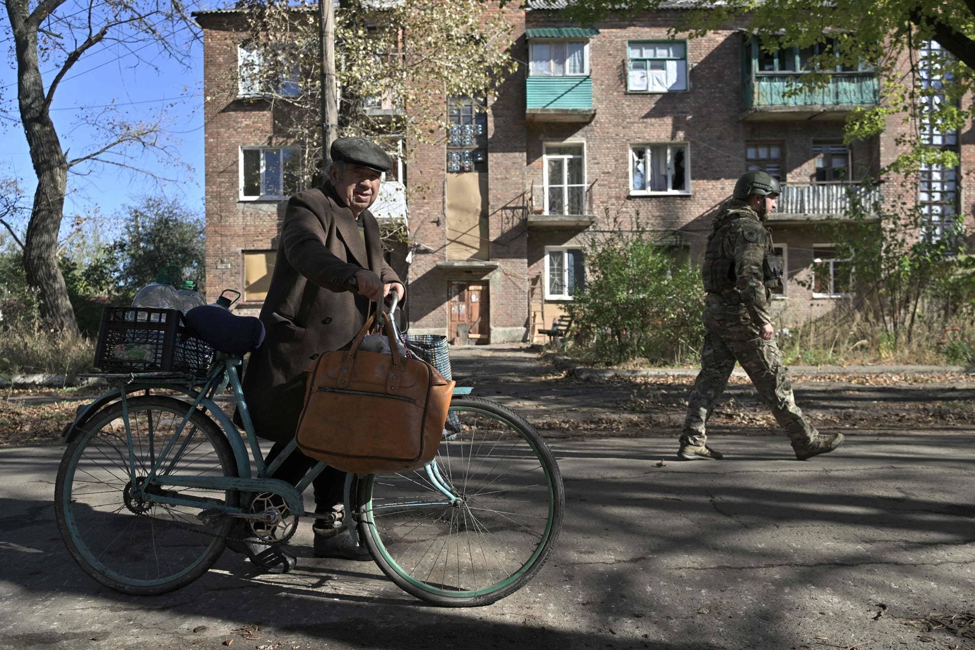 A Ukrainian policeman walks next to local resident pushing his bicycle on a street in the frontline town of Chasiv Yar