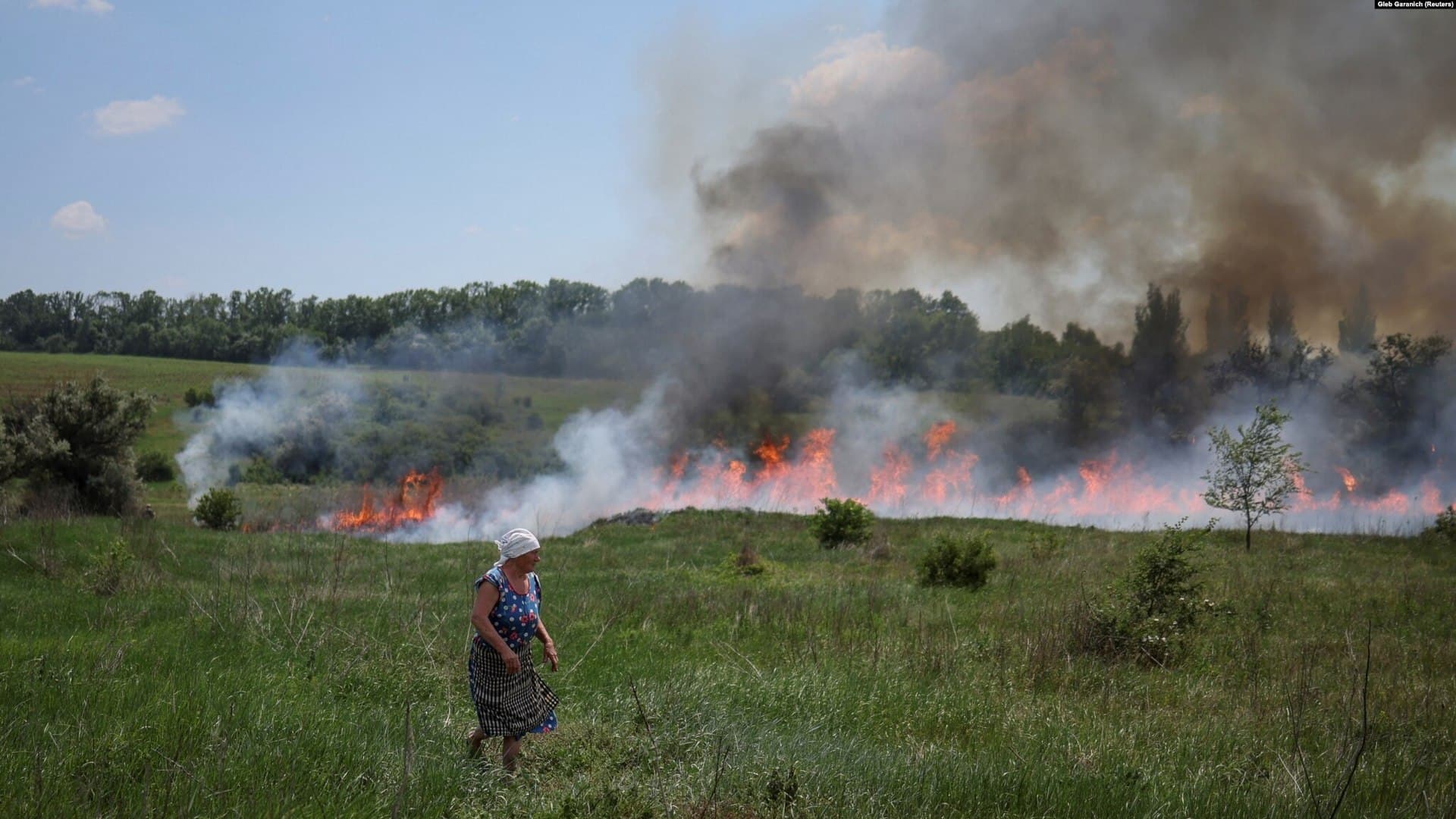 A woman looks on as grass burns after Russian shelling near the town of Bakhmut