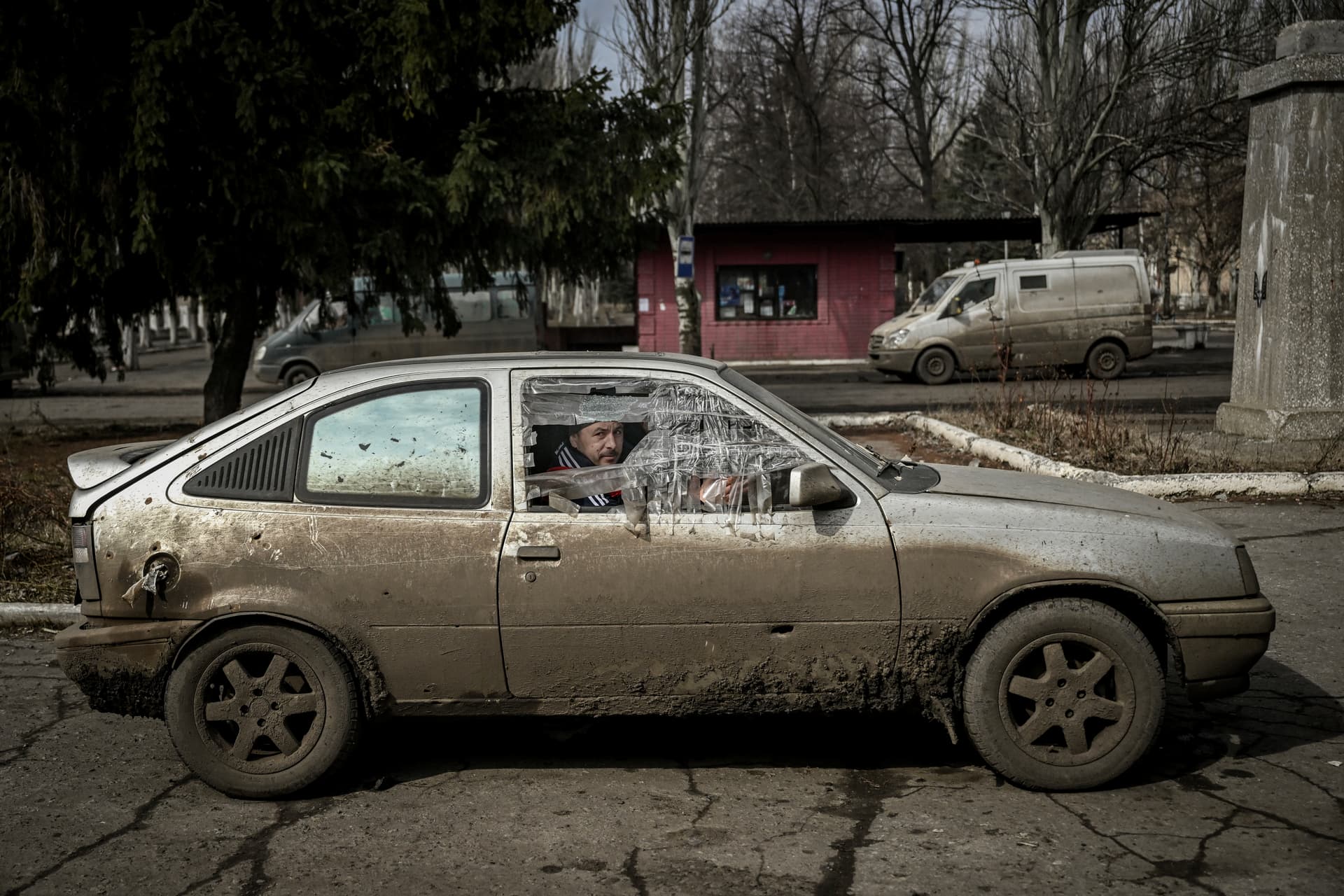 A man looks on as he sits inside a damaged car in the village of Chasiv Yar