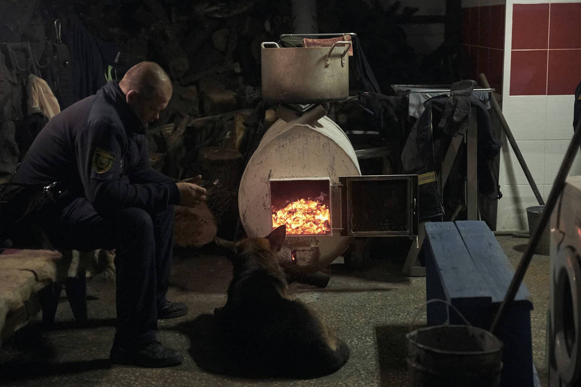 An emergency worker and his dog warm up in front of a wood-burning oven in a shelter in Bakhmut