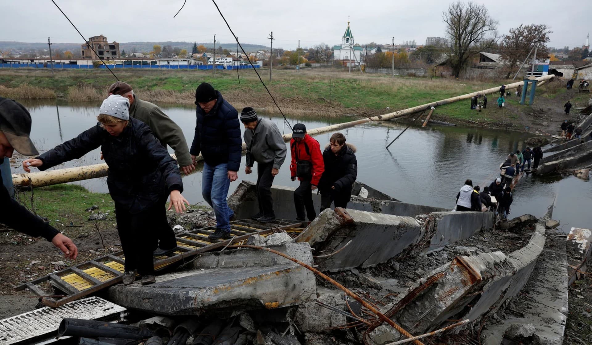 People leave and return to their shelters as they cross a destroyed bridge in Bakhmut