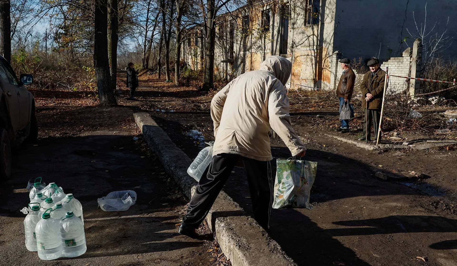 A local resident take bottles with drinking water from humanitarian aid delivered by volunteers, at the side of a damaged residential building in the town of Chasiv Yar, Donetsk Region, Ukraine, November 8, 2023.