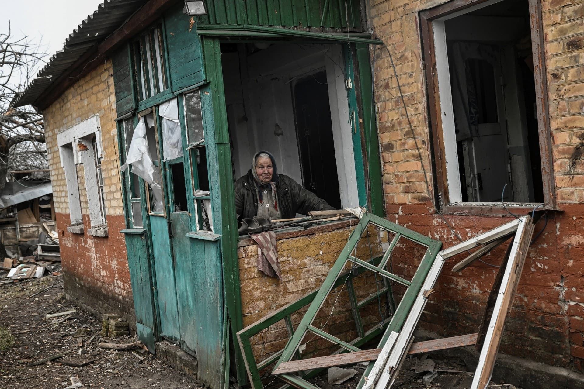 An eldery woman stands behind a window in her damaged house after a shelling in the village of Chasiv Yar
