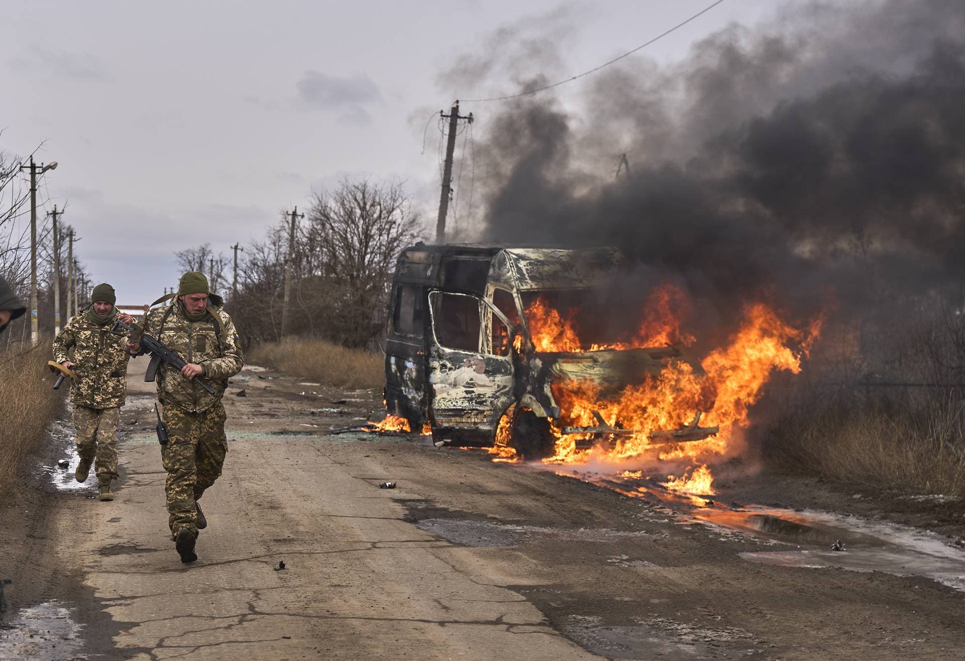 Ukrainian soldiers pass by a volunteer bus burning after a Russian drone hit it near Bakhmut