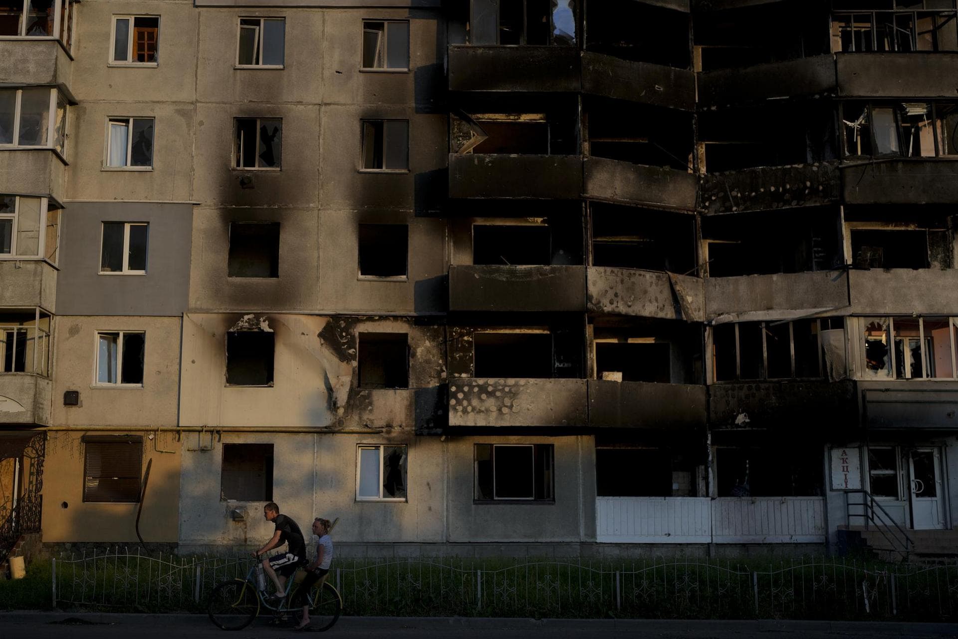 A man rides a bicycle in front of a building destroyed by attacks in Borodyanka