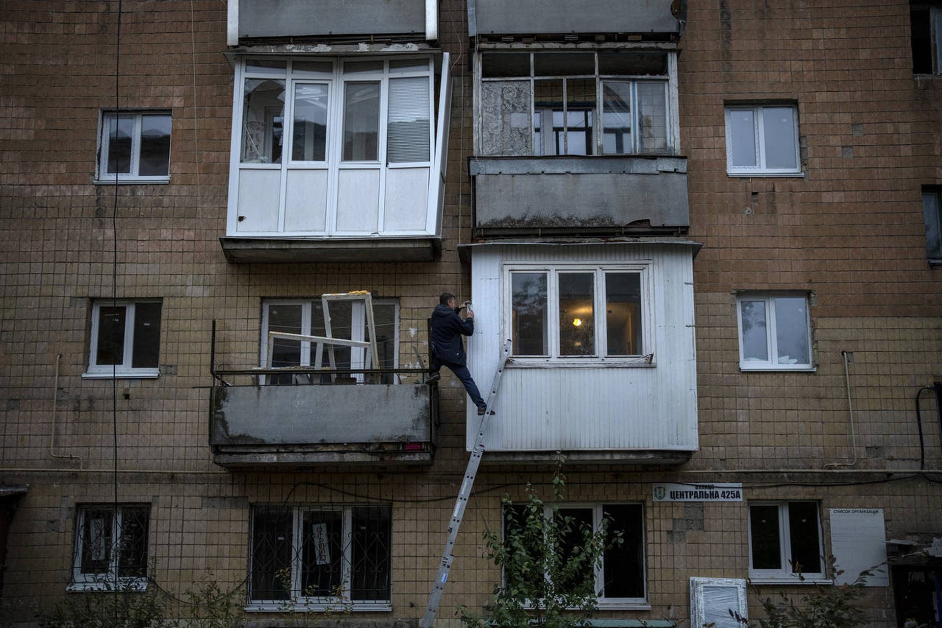A man repairs his balcony on a building damaged by fighting between Ukrainian and Russian forces in Borodyanka