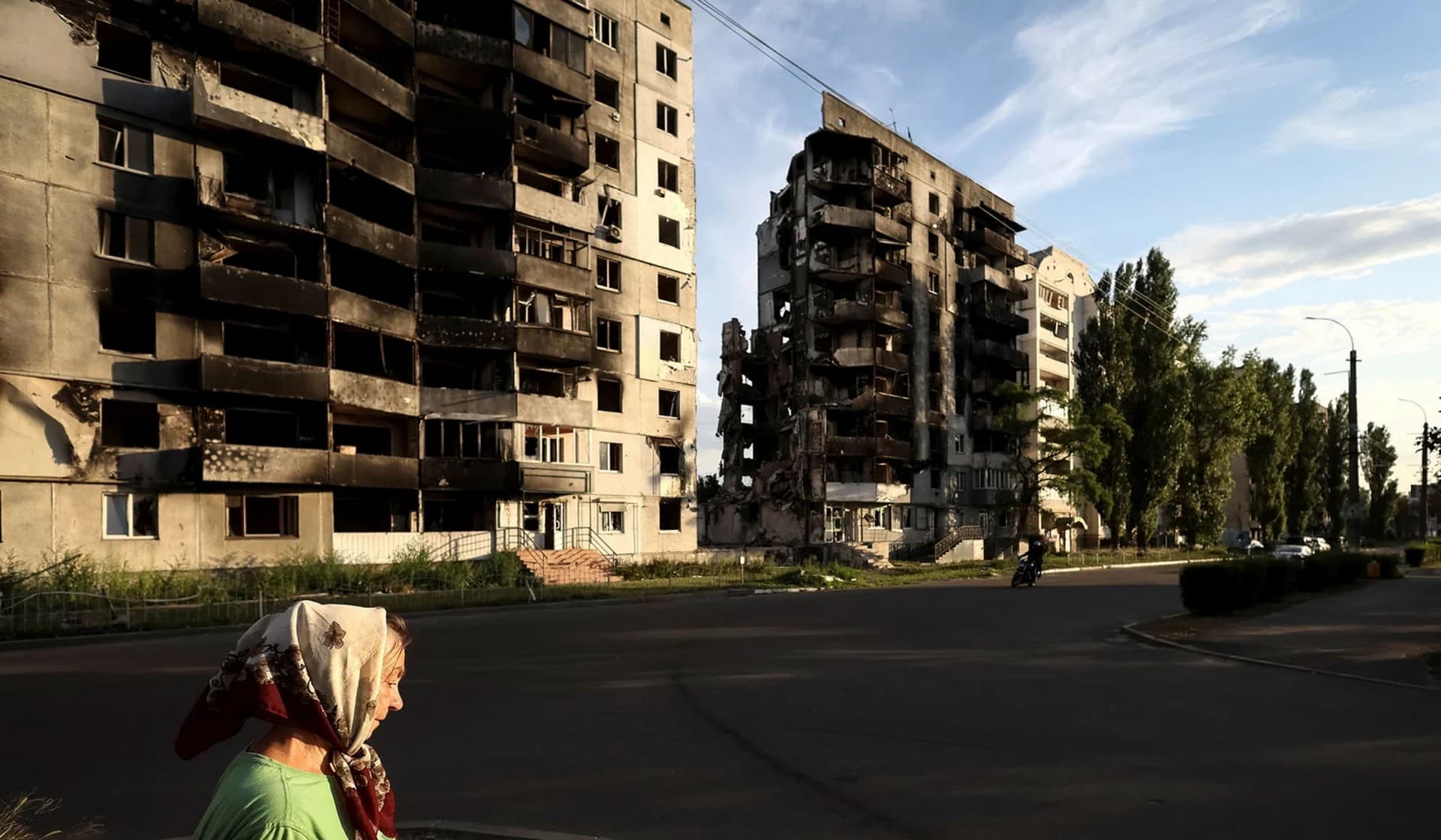 A woman walks down a street in front of destroyed buildings in Borodianka