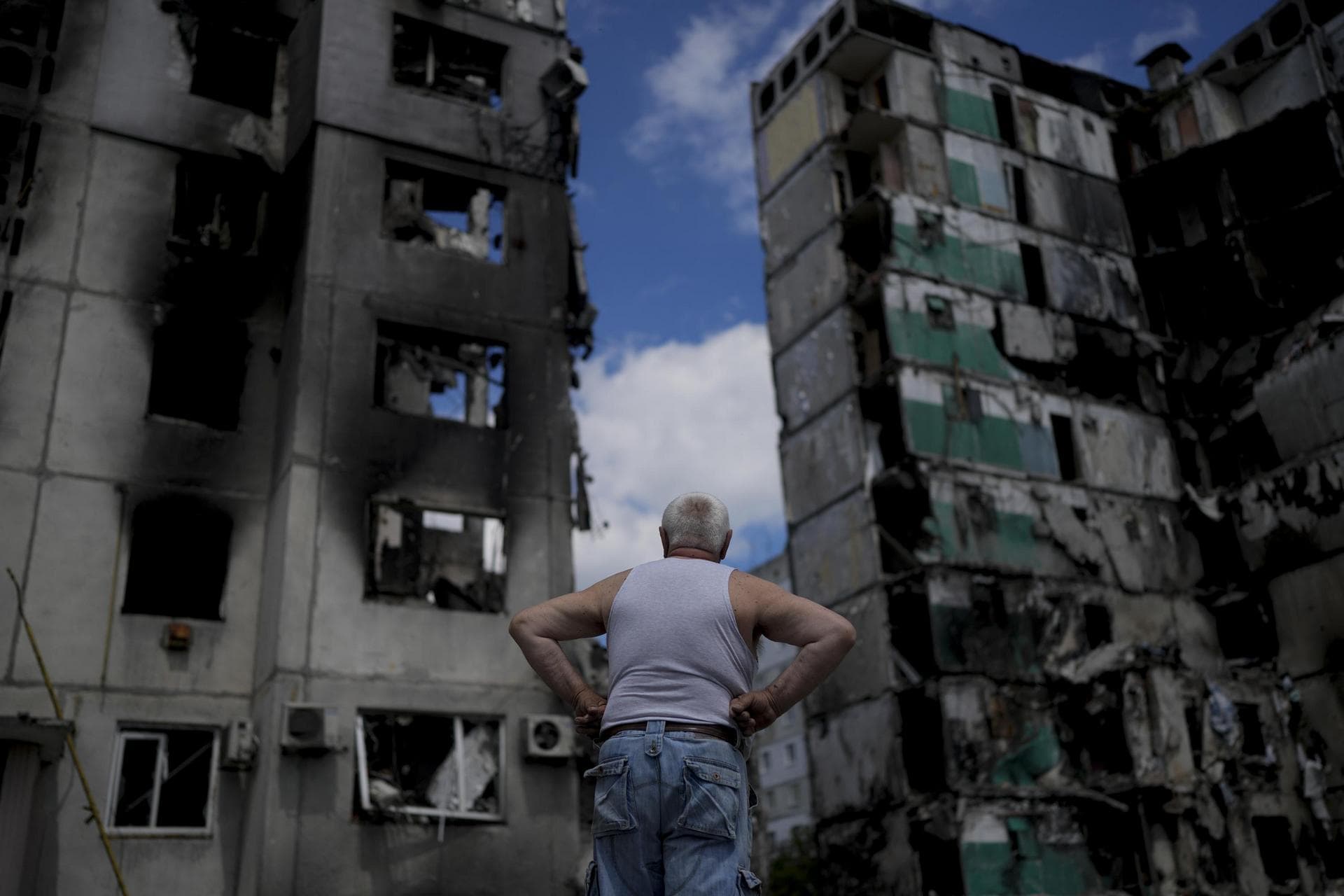 A man stands looking at a building destroyed during attacks, in Borodyanka