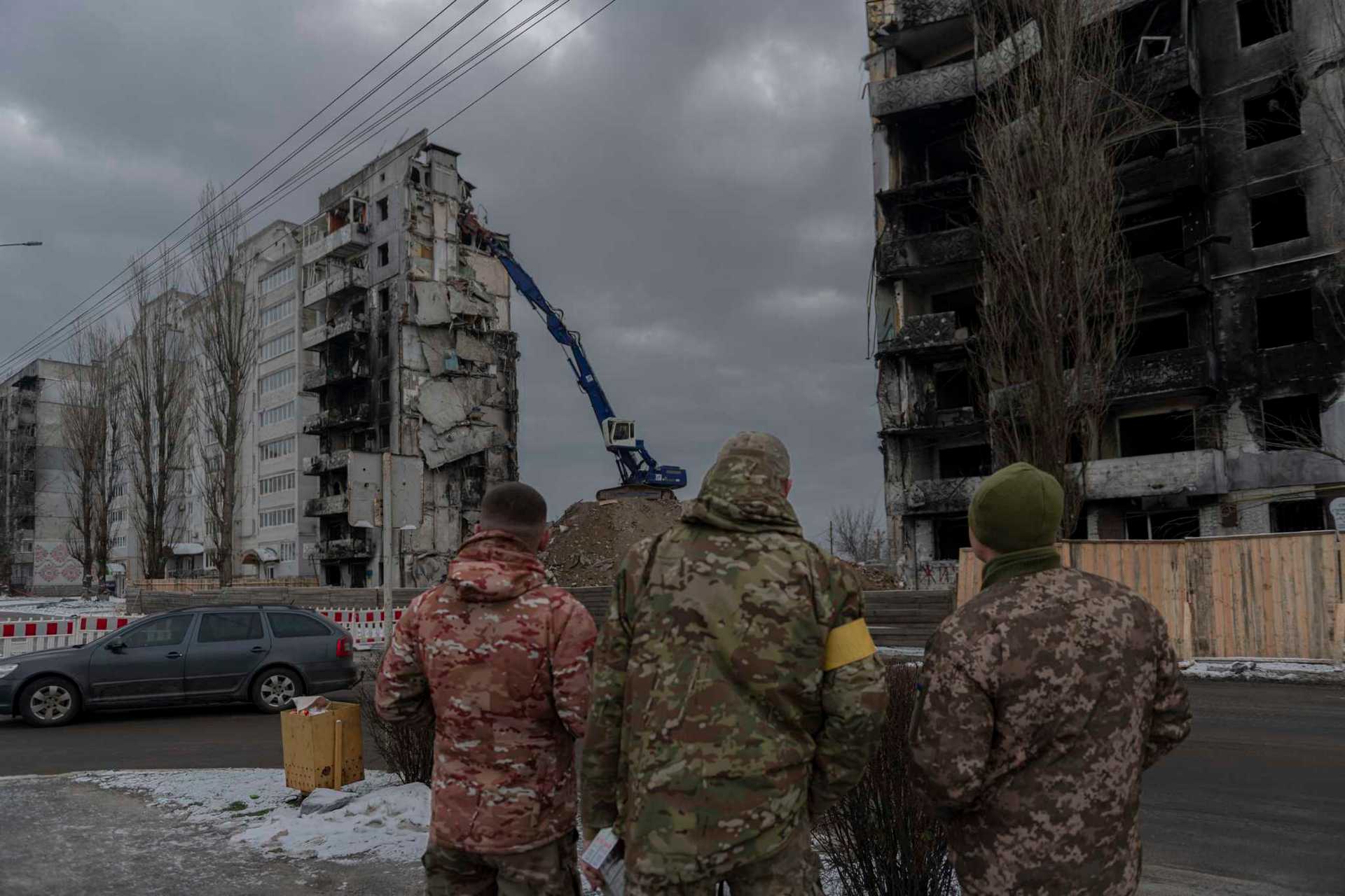 Servicemen watch as a bombed building is dismantled in Borodyanka