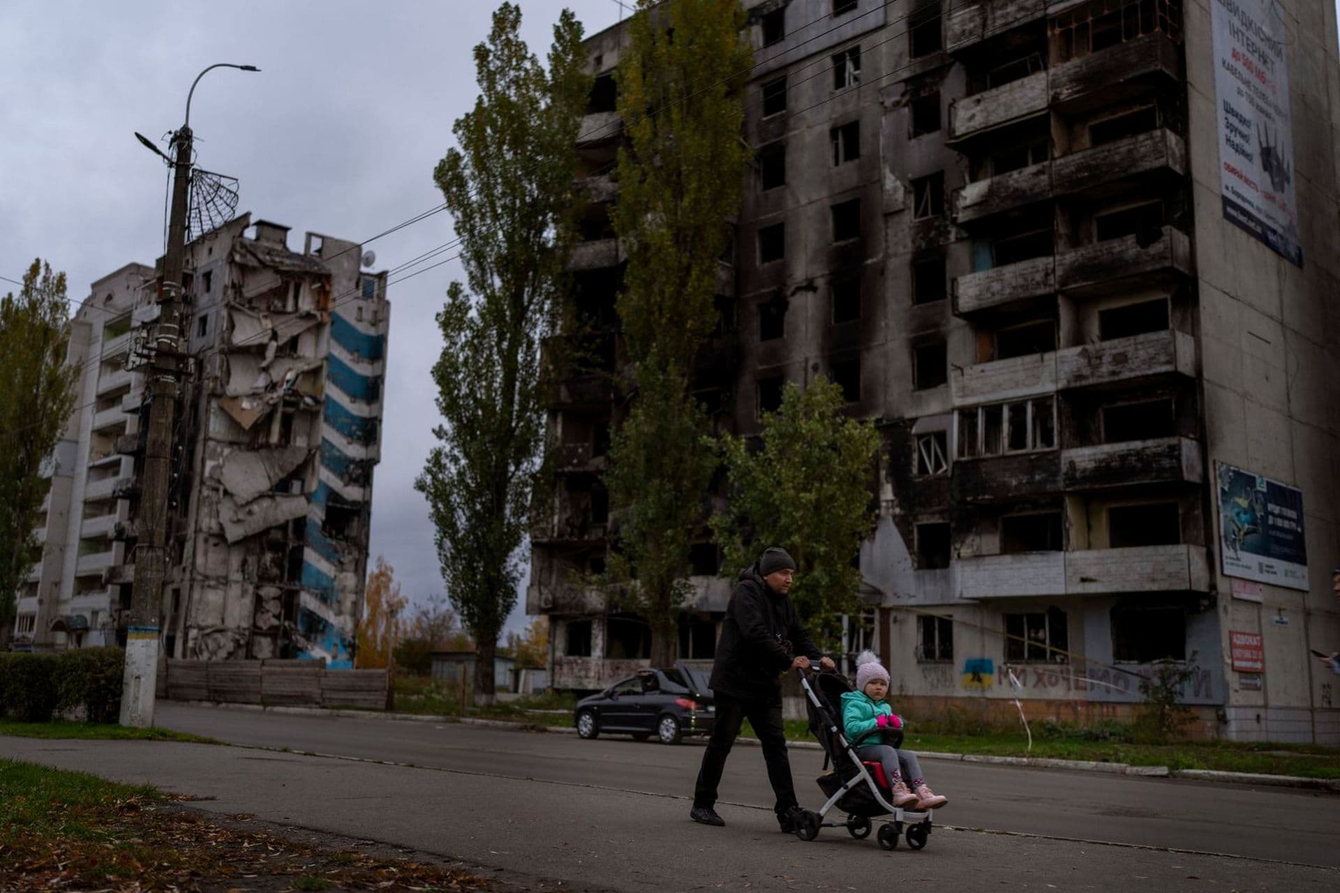 A man pushing a stroller walks past a building damaged by fighting between Ukrainian and Russian forces in Borodyanka