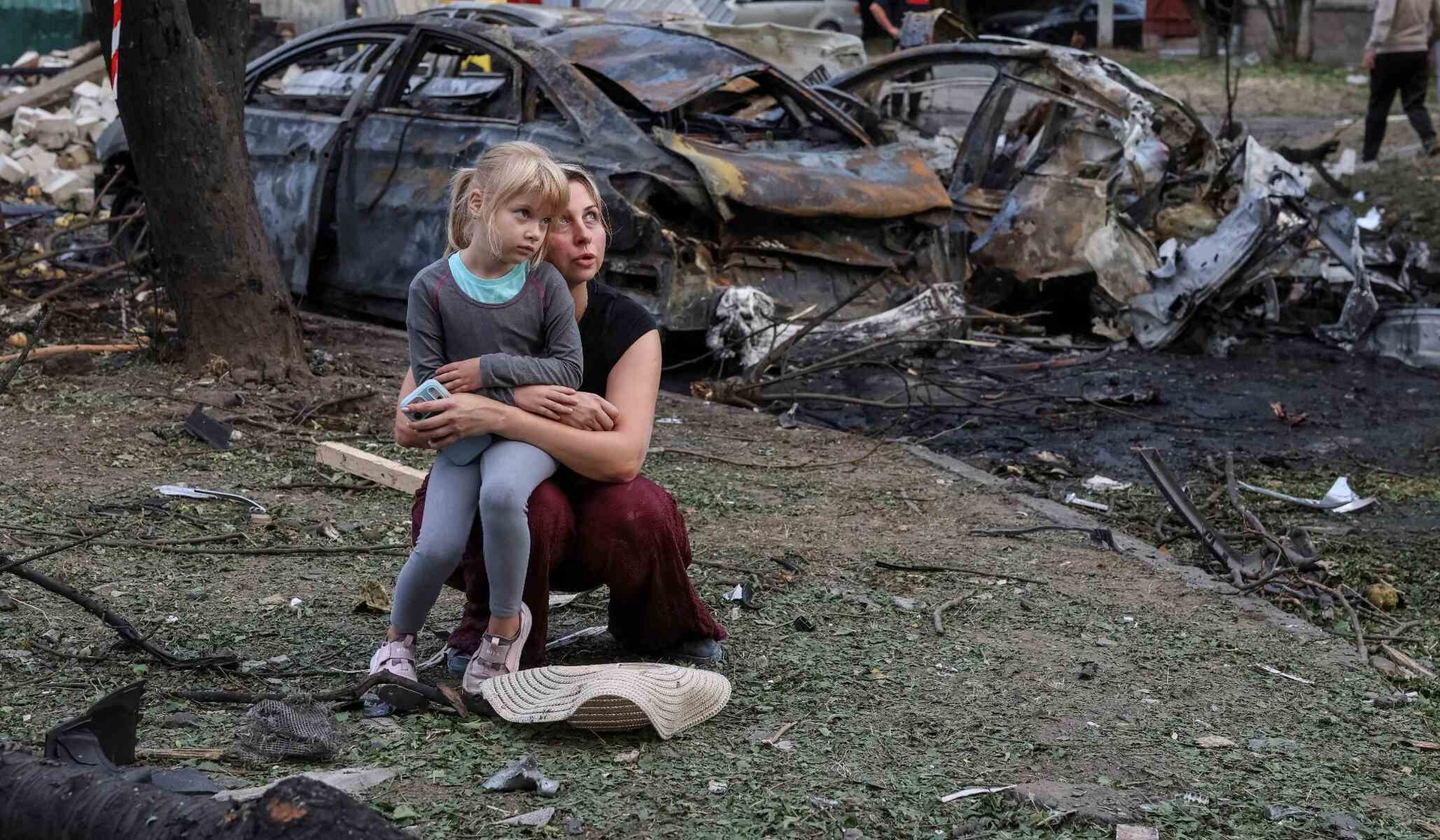 A mother and daughter sit at a site of an apartment building damaged by a Russian missile strike in Borispil