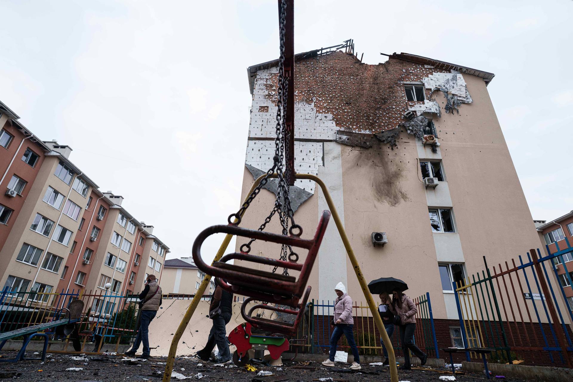 People walk in front of a house which was damaged after a Russian strike on residential neighbourhood in Kriukivshchyna