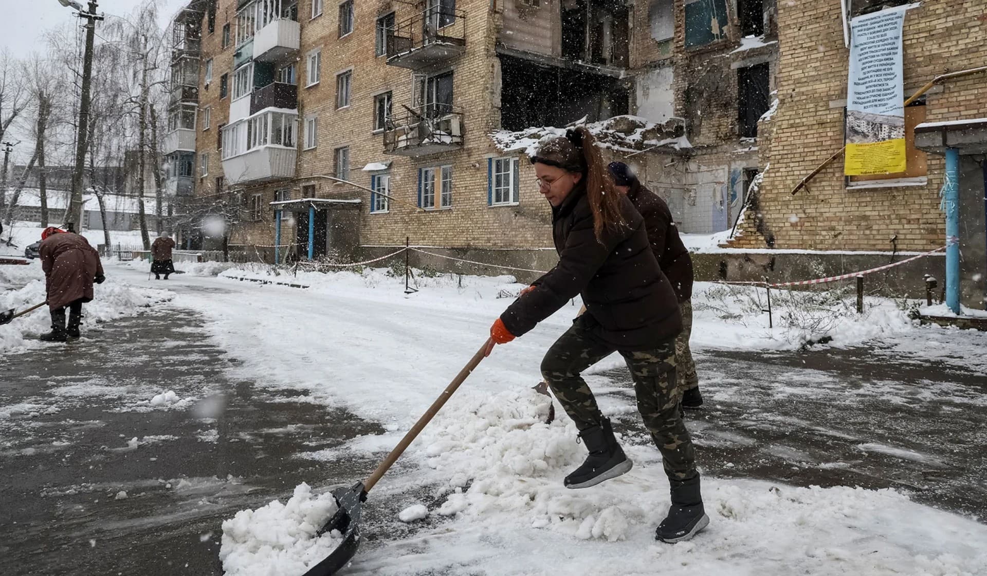 Local resident Tetiana Reznychenko, 43, shovels snow near her destroyed building, which has no electricity, heating and water, in the village of Horenka