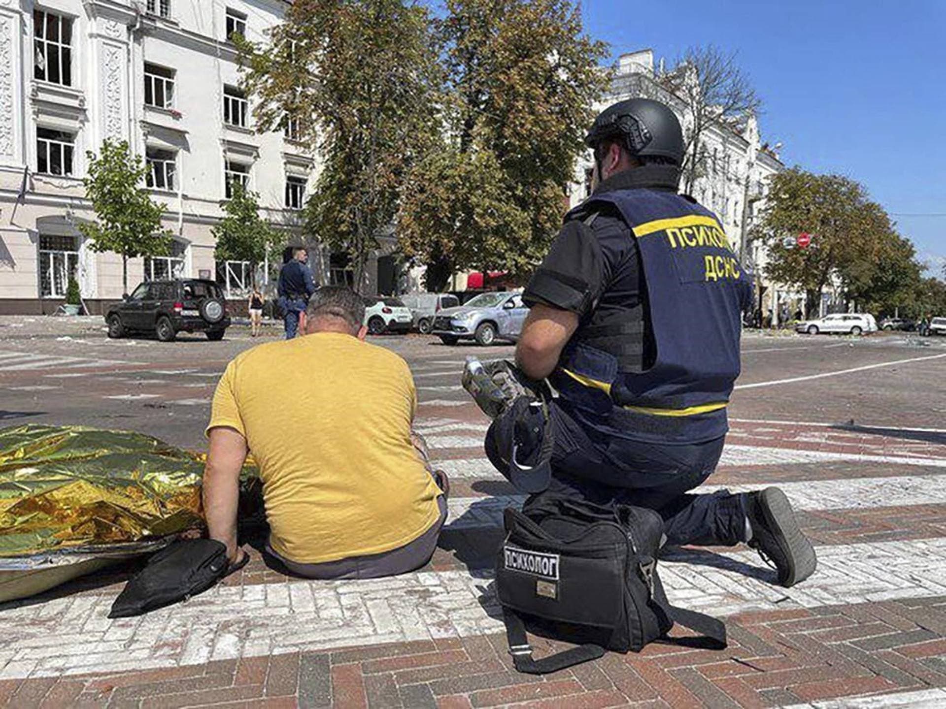 a man sits near a covered dead body after Russian attack in Chernihiv