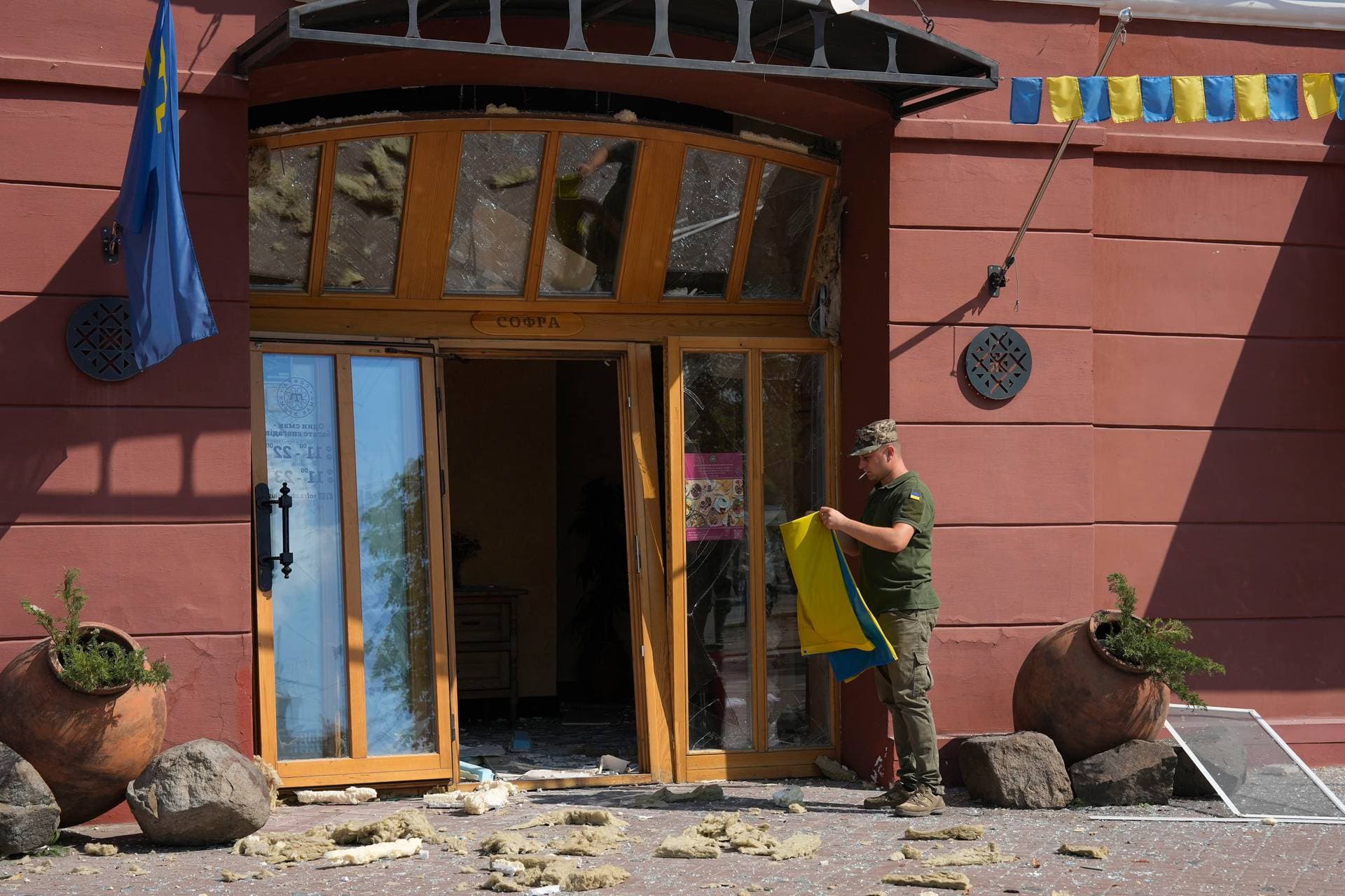 Ukrainian serviceman holds a Ukrainian flag next to the entrance of a restaurant damaged by a Russian attack in Chernihiv