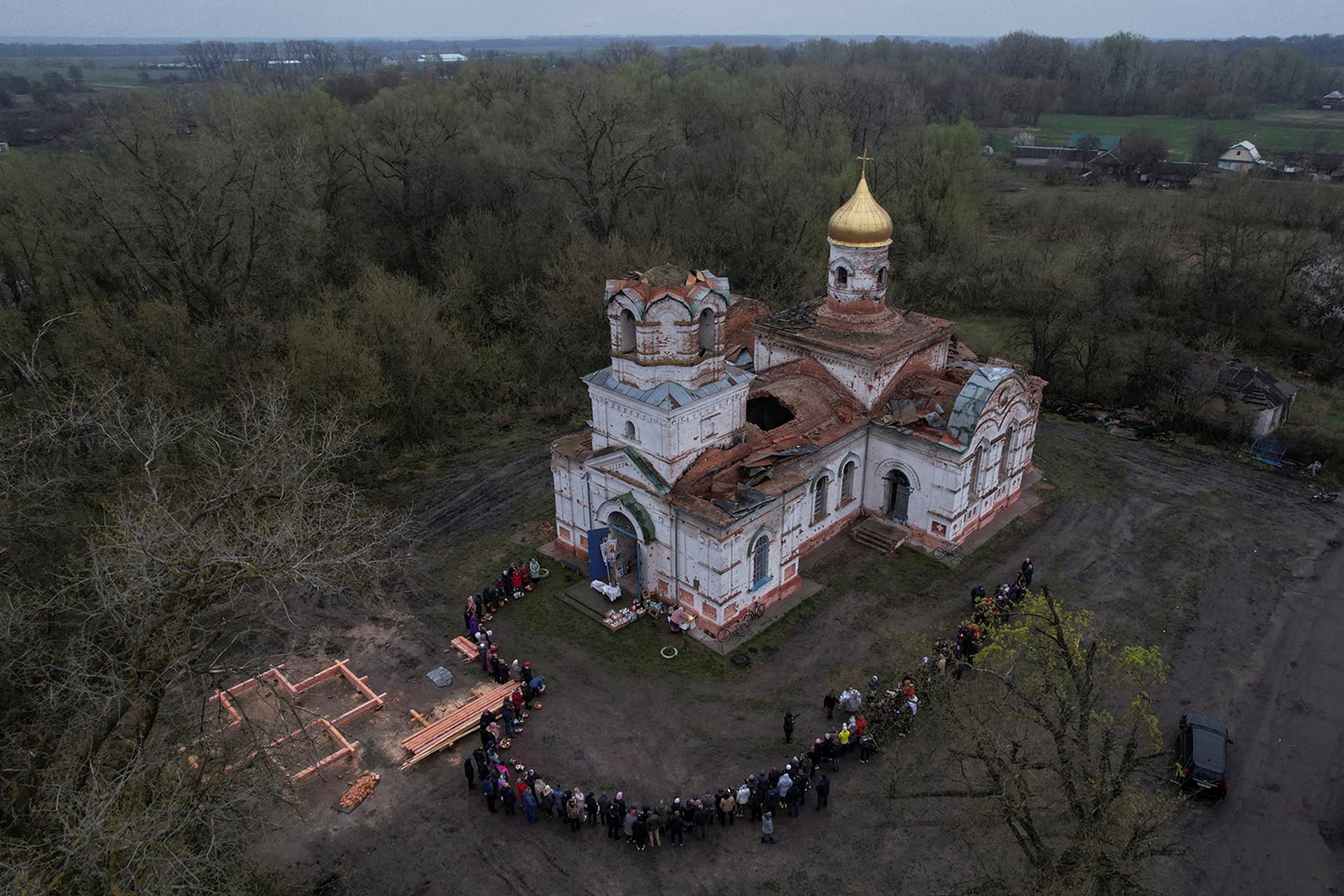 An Orthodox priest sprays holy water on believers outside a church damaged by a Russian attack in the village of Lukashivka