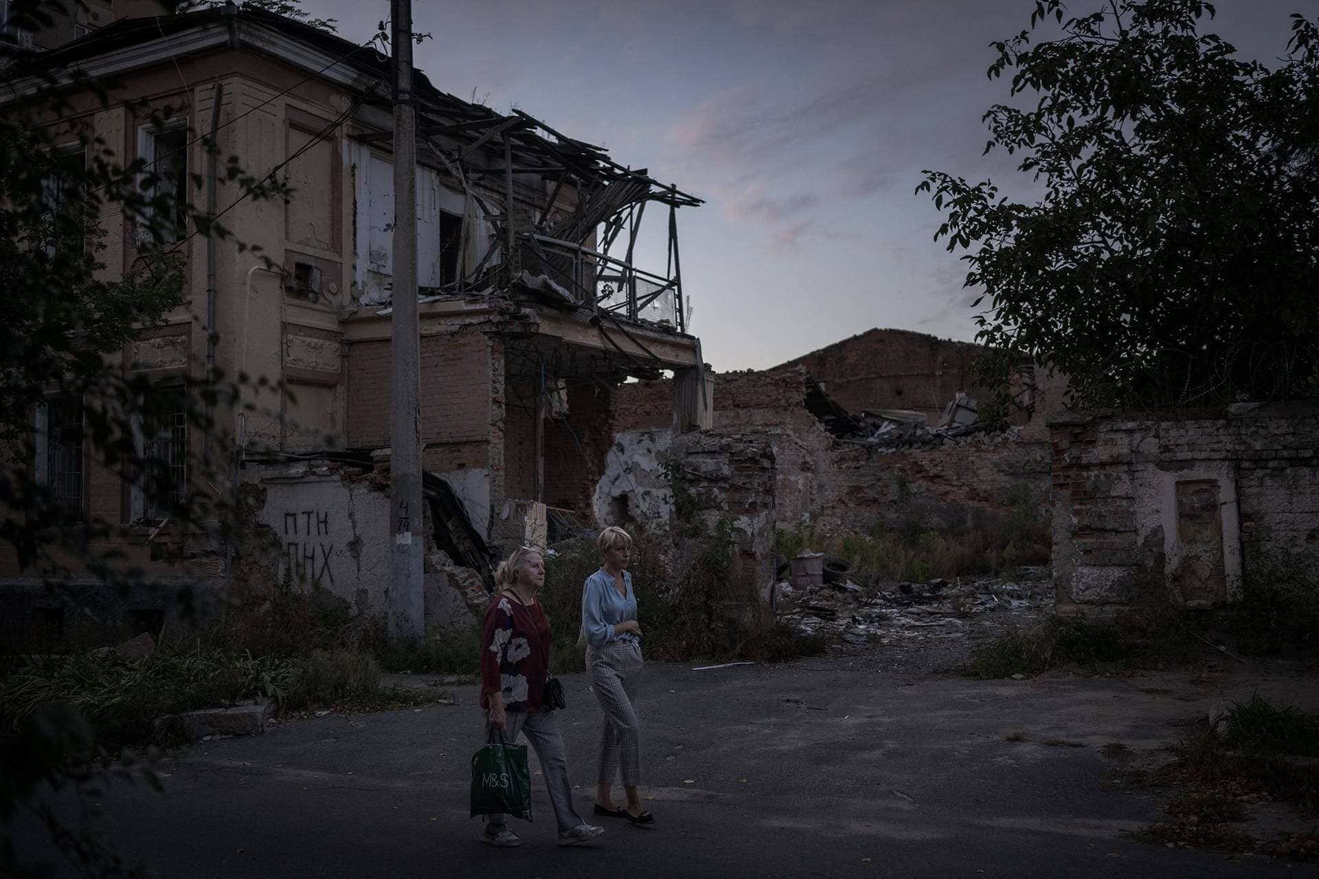 Residents of Stary Saltov walk past a destroyed house