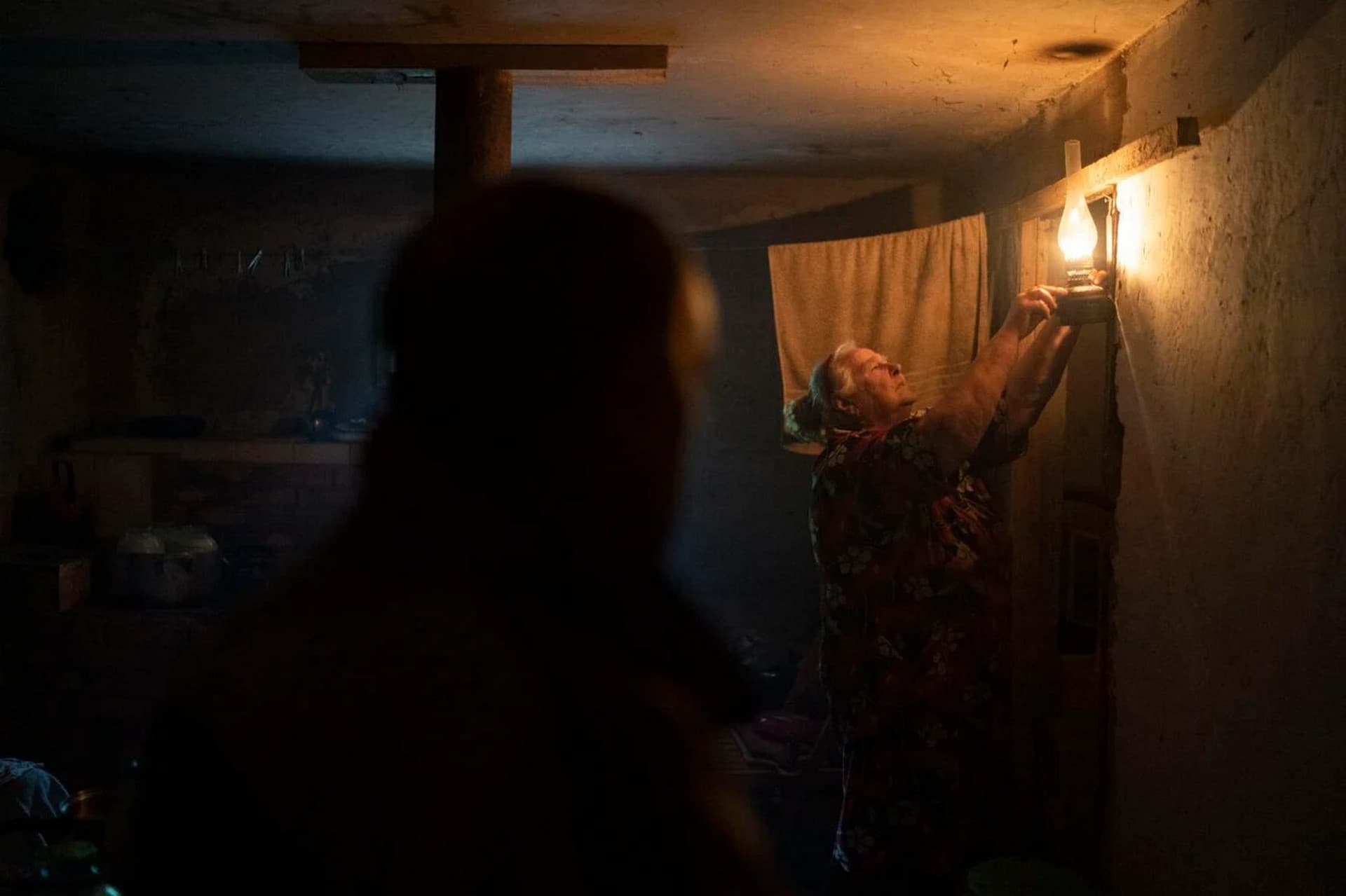 Liudmyla Dmyttruk lights up an oil lamp, as she shows the basement where she is living together with her neighbors in the freed village of Hrakove