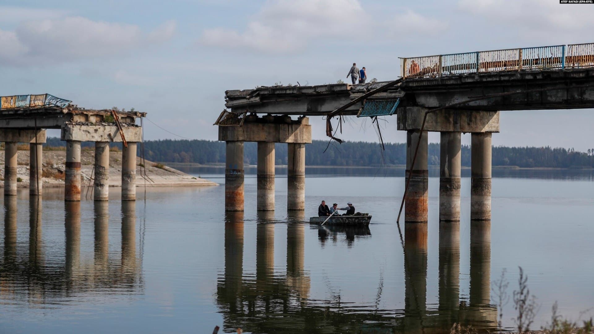 People transport fuel on a boat in front of a destroyed bridge across the Siverskyi-Donets river in Staryi-Saltiv