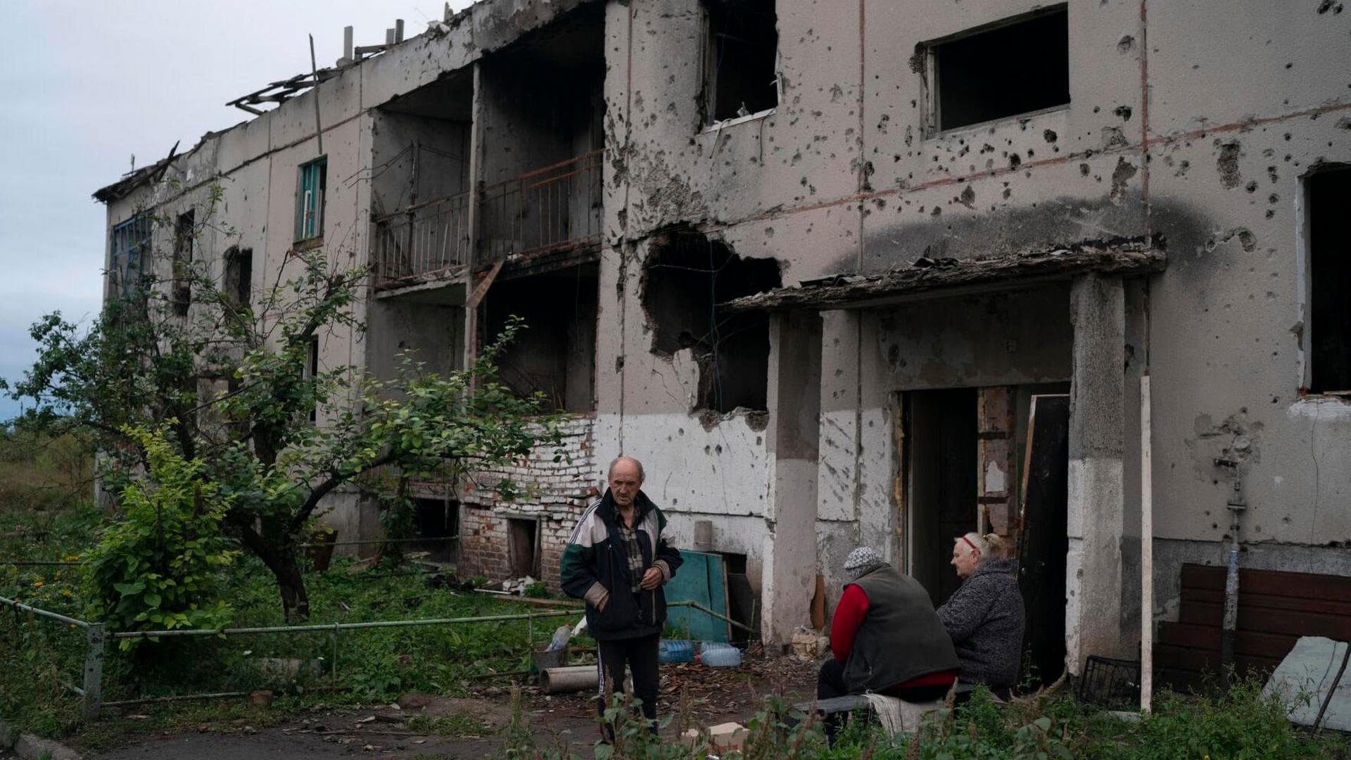 Oleh Lutsai stands with his neighbors at the entrance of their damaged residential building in the freed village of Hrakove