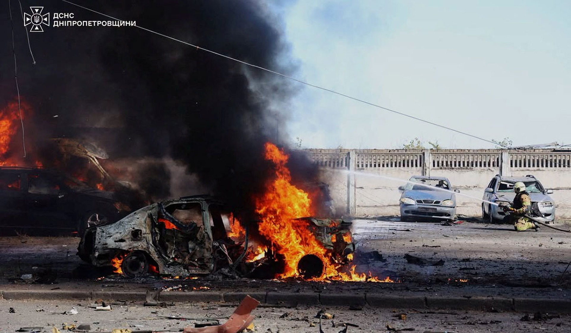 A rescuer extinguishes a burning car at a site of a Russian drone strike in Dnipro