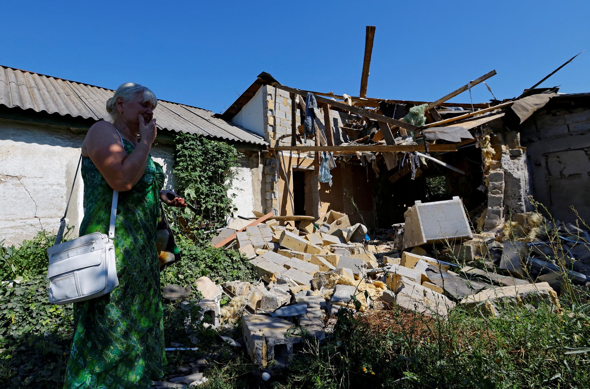 woman reacts next to the damaged house of her son in Donetsk