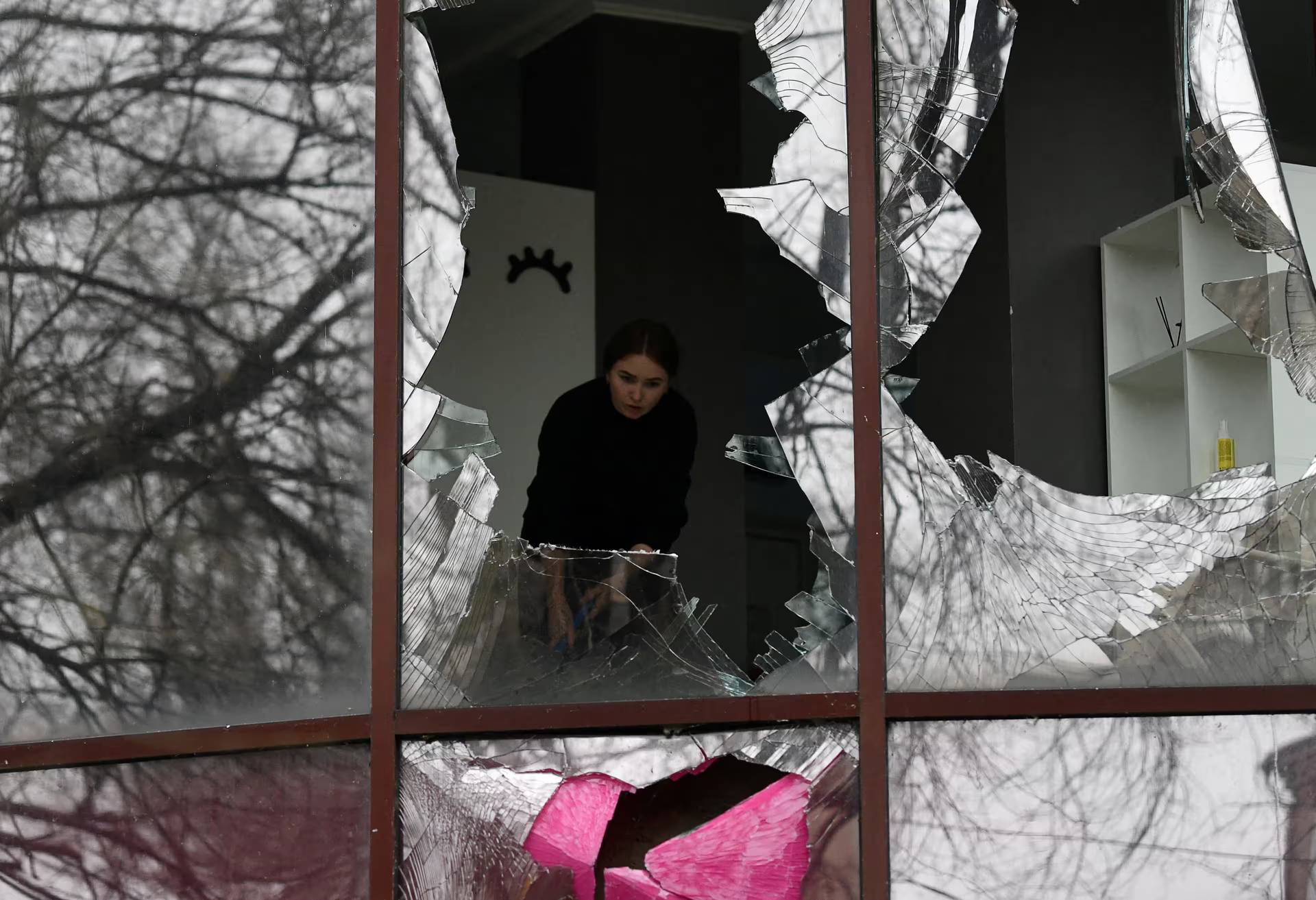 A woman removes shards of glass from broken windows of a beauty salon, following recent shelling in Donetsk