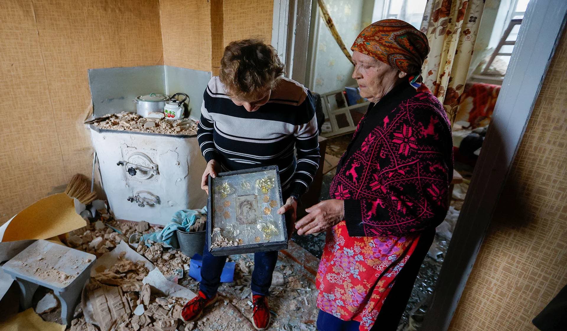 Local resident holds an icon as her mother stands nearby inside their house destroyed by shelling in Donetsk