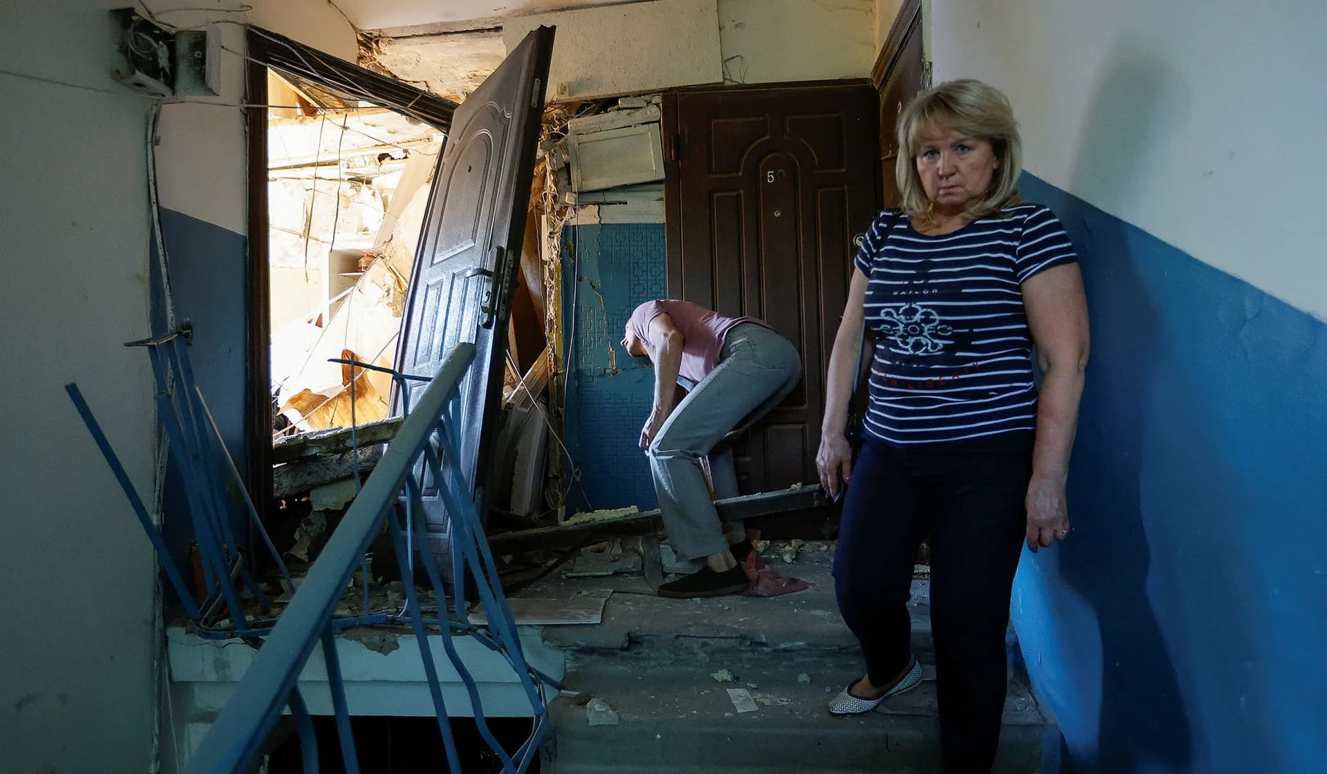 Retired employee stands on a staircase of a multi-story building next to her apartment destroyed in recent shelling in Donetsk